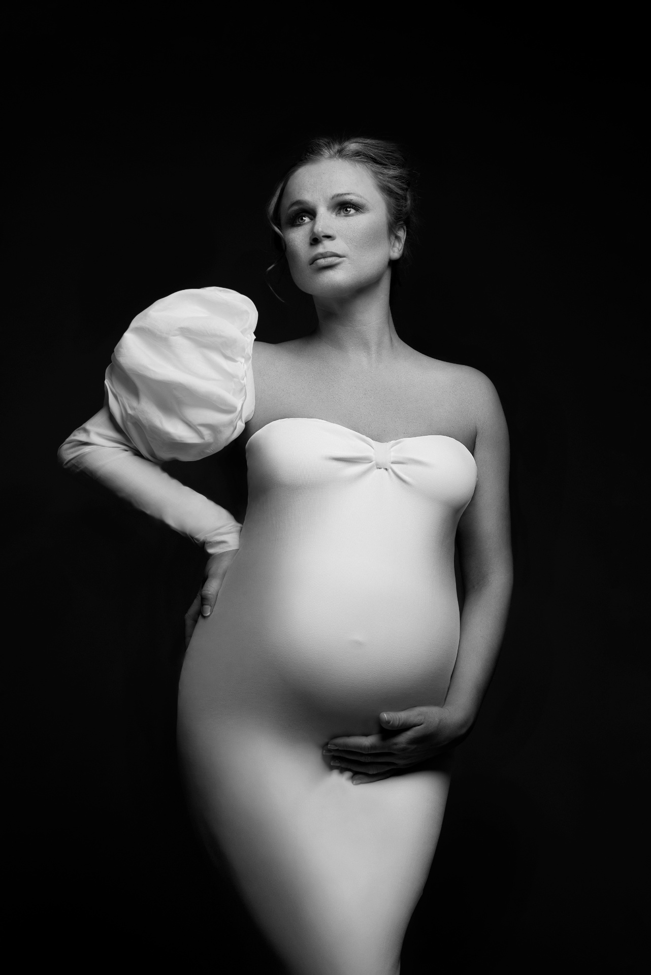 Ritratto elegante di maternità in bianco e nero a Bologna firmato Claudia Spaziani: abito aderente con manica a sbuffo e sfondo scuro, stile sofisticato.