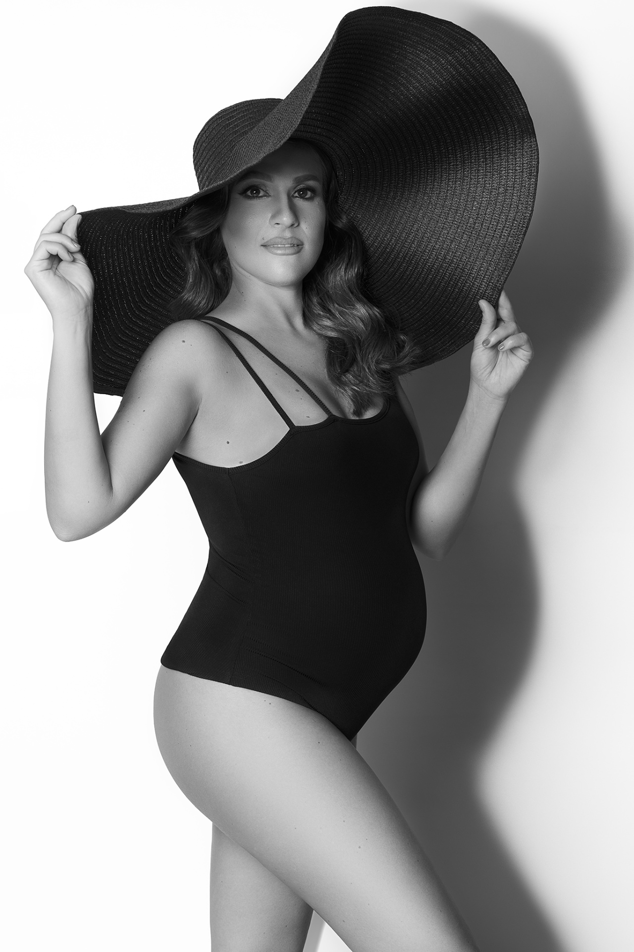 Foto moda maternità in bianco e nero a Bologna realizzata da Claudia Spaziani: donna incinta con cappello a tesa larga e bodysuit, stile fashion e deciso.
