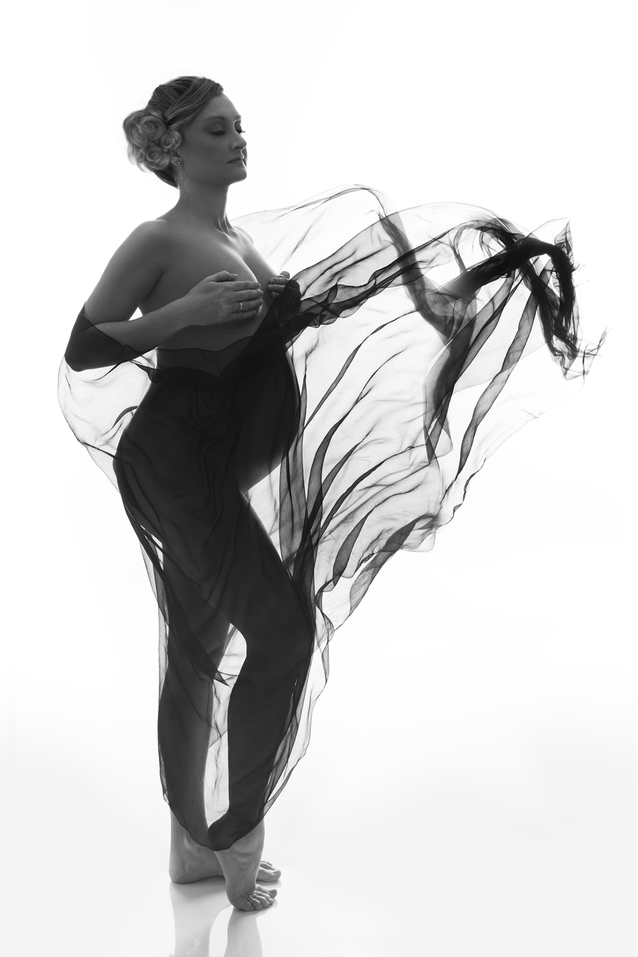 Ritratto artistico in bianco e nero di maternità a Bologna con Claudia Spaziani: donna incinta avvolta in tessuto trasparente in movimento, stile etereo.