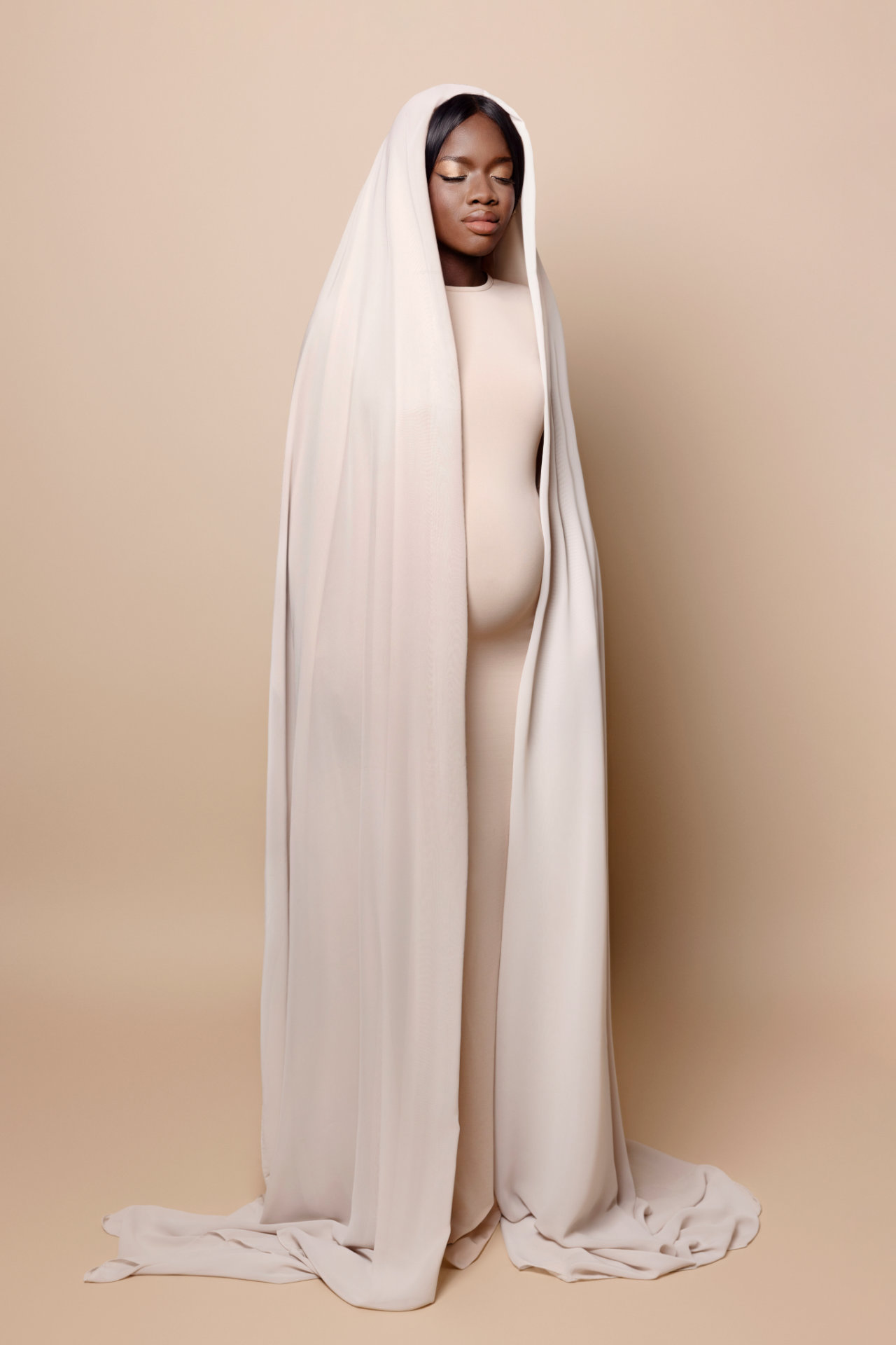 Ritratto di maternità realizzato da Claudia Spaziani a Bologna: donna incinta in abito beige con velo lungo, stile minimalista e spirituale.