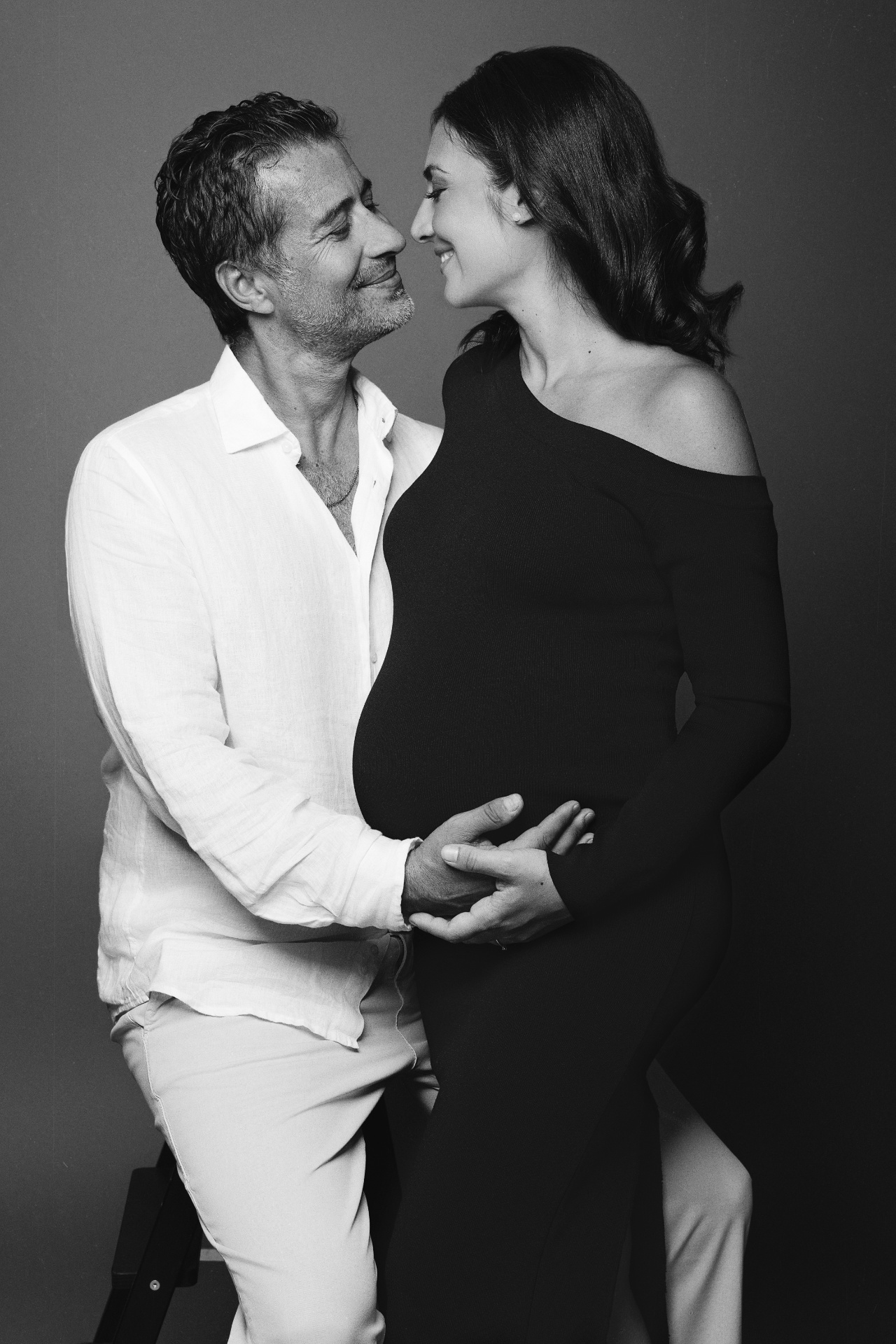 Foto maternità in bianco e nero a Bologna firmata Claudia Spaziani: coppia elegante in posa ravvicinata, mani sulla pancia e sguardi intensi.