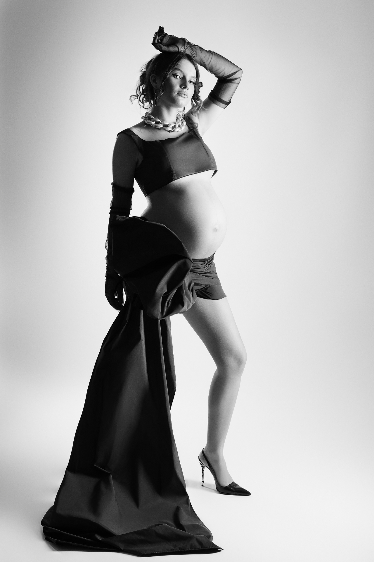 Ritratto di maternità in bianco e nero a Bologna realizzato da Claudia Spaziani: donna incinta in outfit elegante con guanti e tessuto fluente, stile moda e artistico.