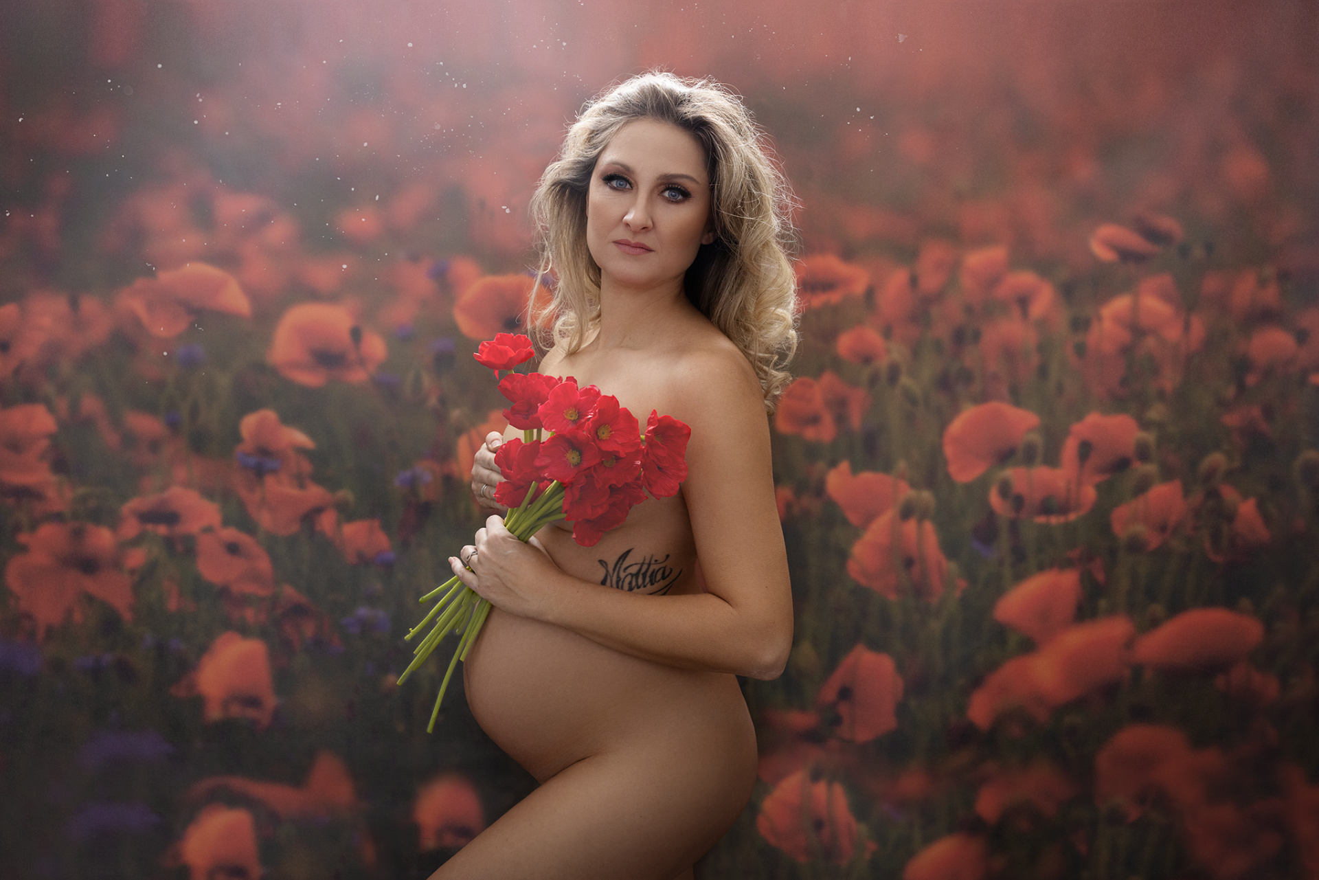 Servizio fotografico maternità floreale a Bologna realizzato da Claudia Spaziani: donna incinta con papaveri rossi e capelli biondi mossi, atmosfera naturale e poetica.