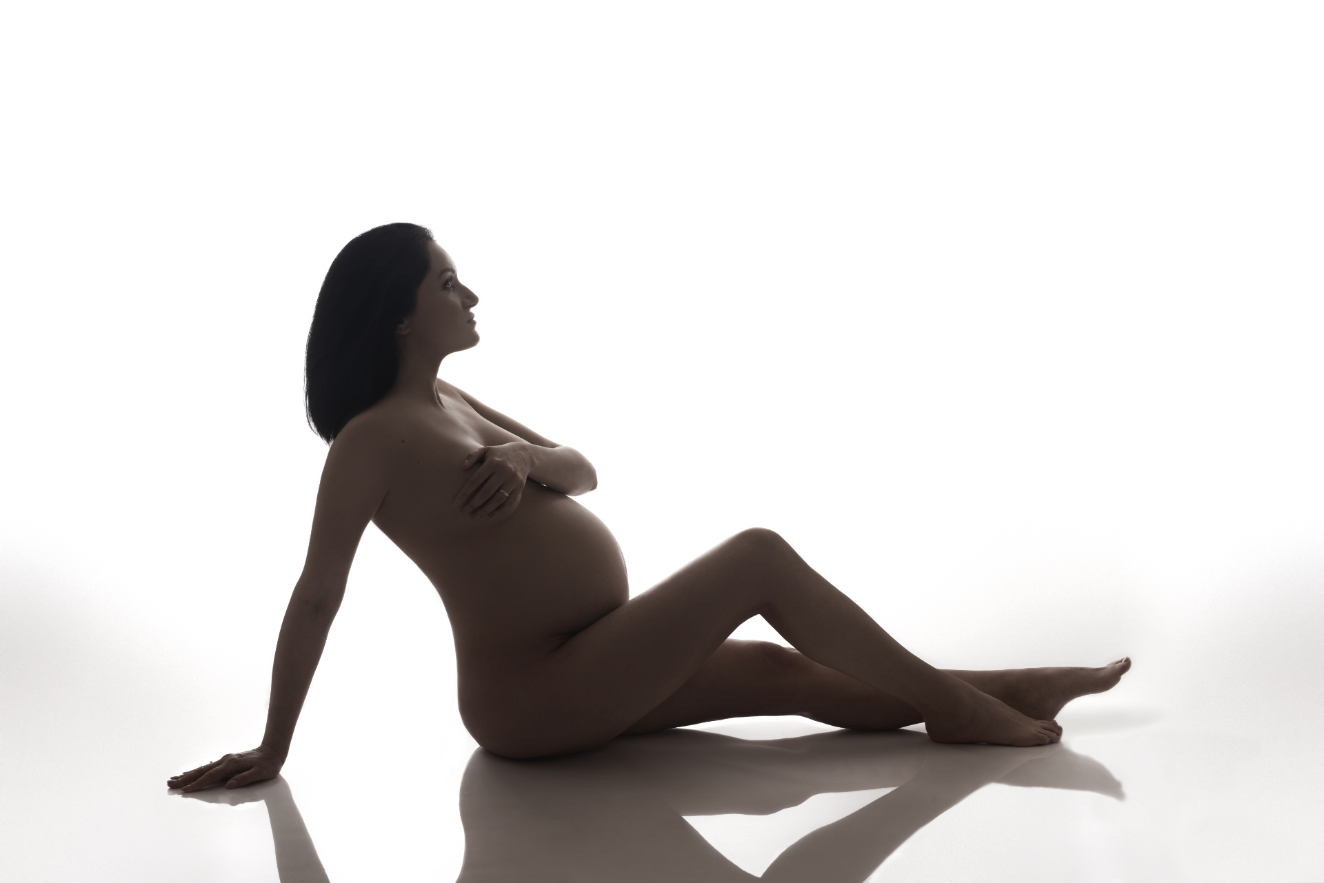 Ritratto artistico di maternità in bianco e nero a Bologna realizzato da Claudia Spaziani: silhouette di donna incinta seduta, luce intensa e atmosfera scultorea.