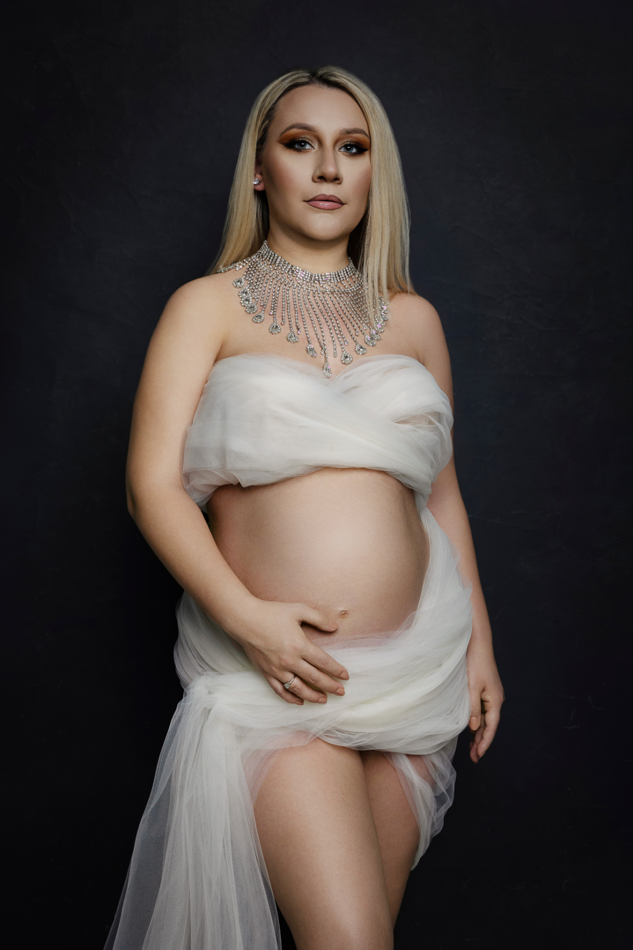 Ritratto di maternità a Bologna realizzato da Claudia Spaziani: donna incinta in tessuto bianco trasparente con collana argento, atmosfera elegante e serena.