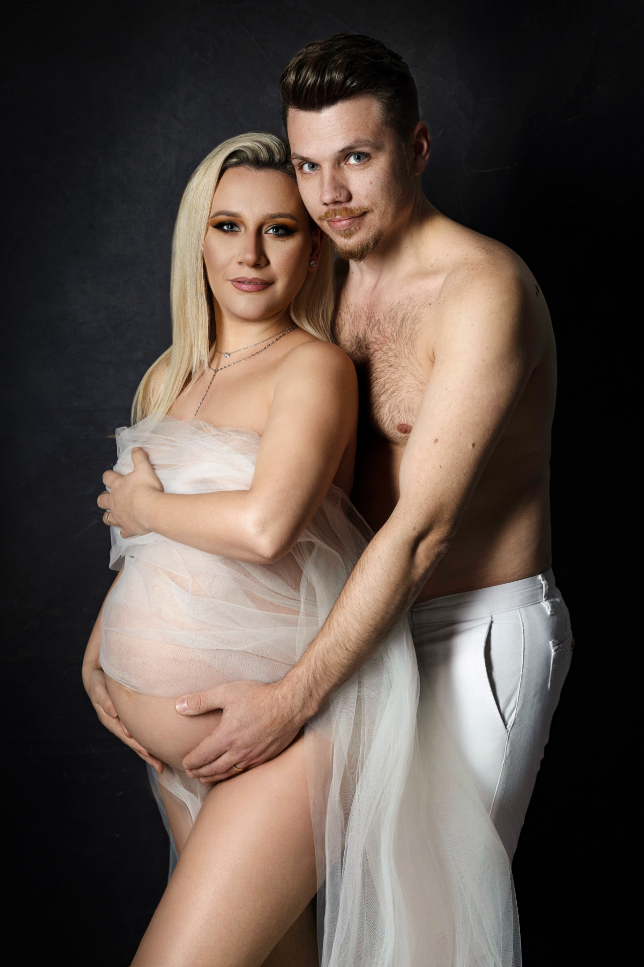 Servizio fotografico maternità a Bologna con Claudia Spaziani: coppia avvolta in tessuti bianchi trasparenti, posa intima e affettuosa.