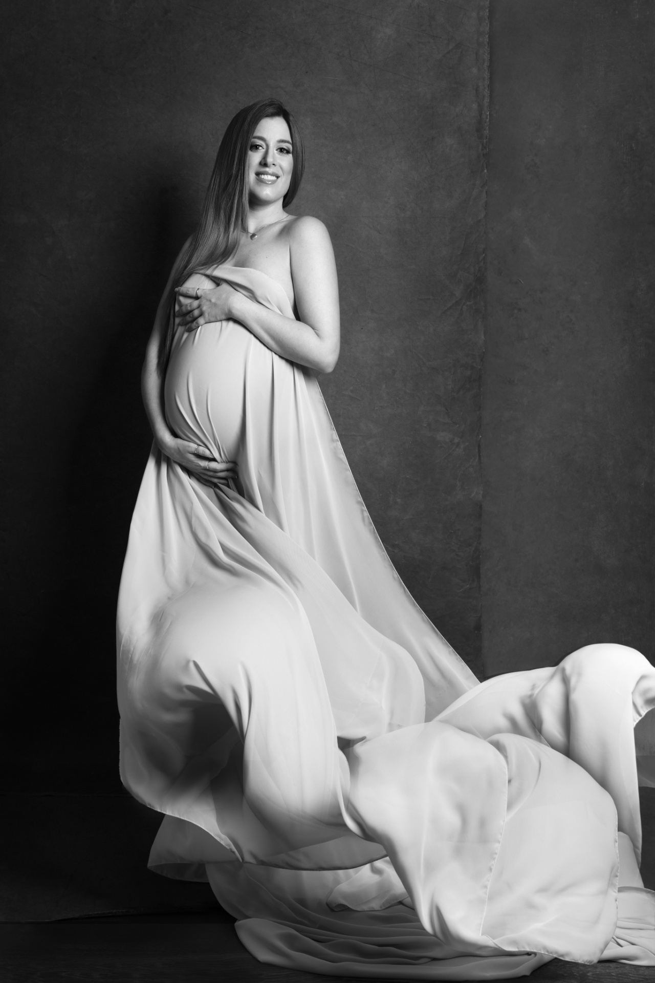 Foto artistica in bianco e nero di maternità a Bologna con Claudia Spaziani: donna incinta avvolta in tessuto fluente, posa dinamica e drammatica.