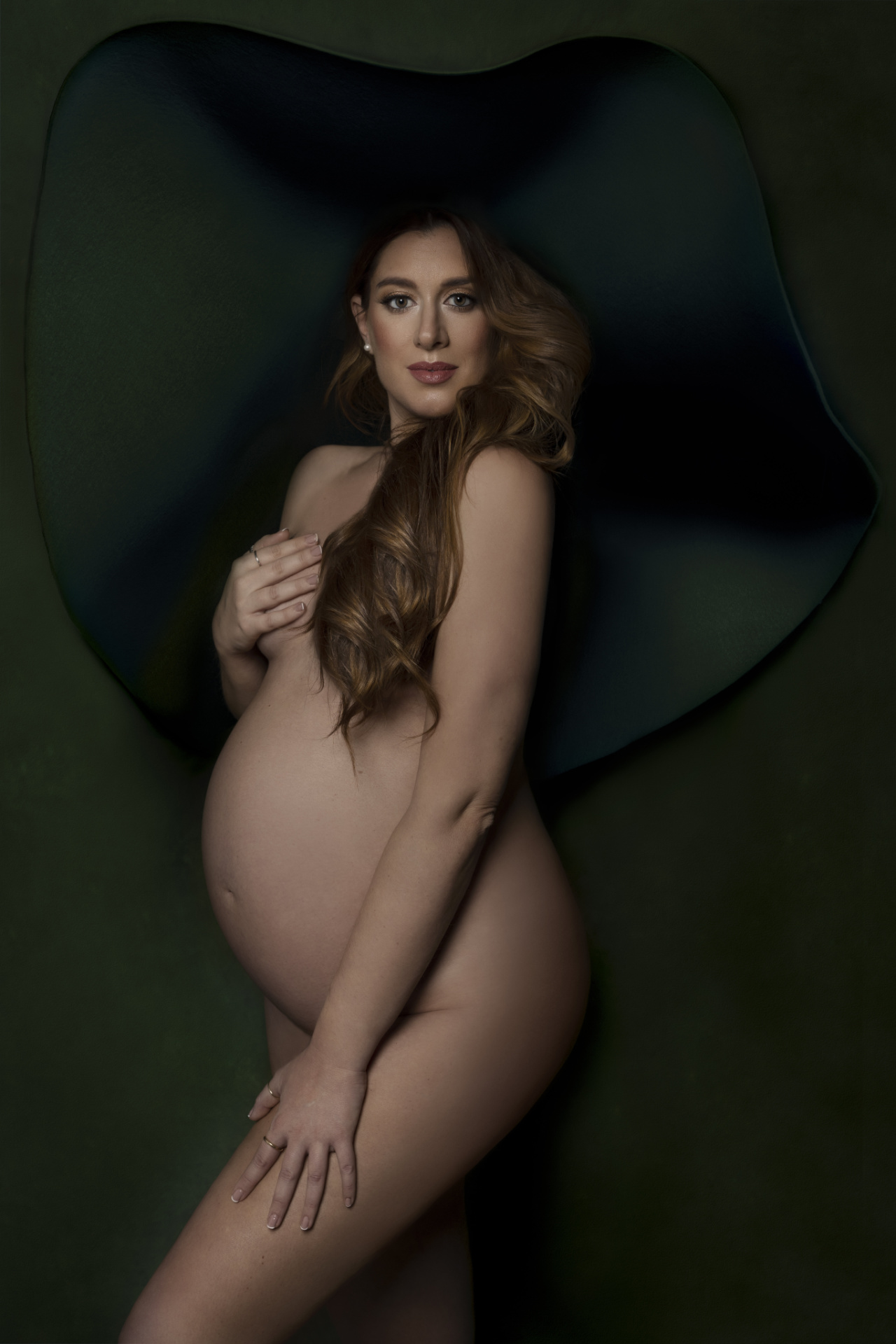 Servizio fotografico maternità a Bologna realizzato da Claudia Spaziani: donna incinta con copricapo verde scultoreo, posa artistica e raffinata.