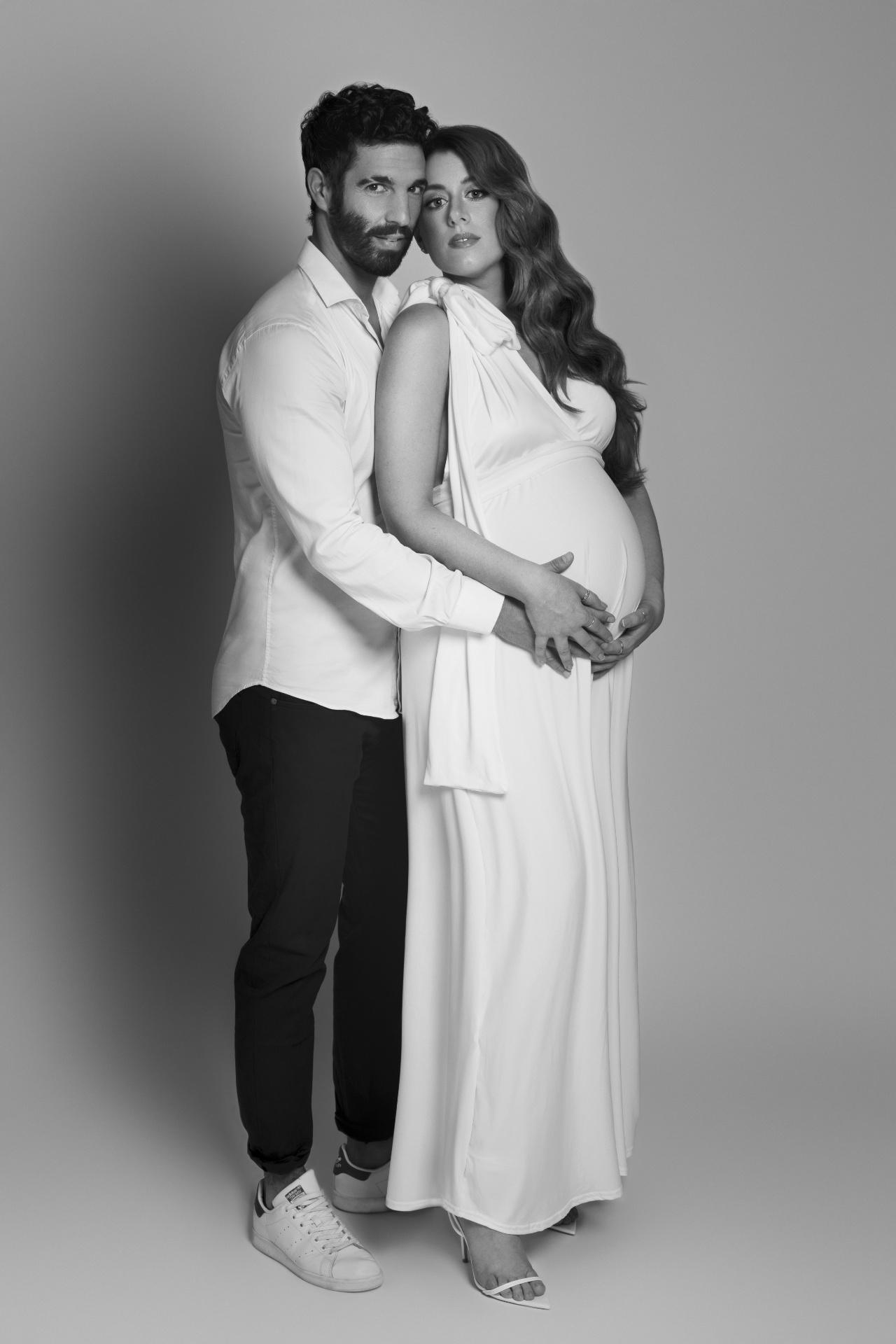 Foto di coppia maternità in bianco e nero a Bologna con Claudia Spaziani: donna incinta in abito bianco elegante e partner in camicia, posa intima.