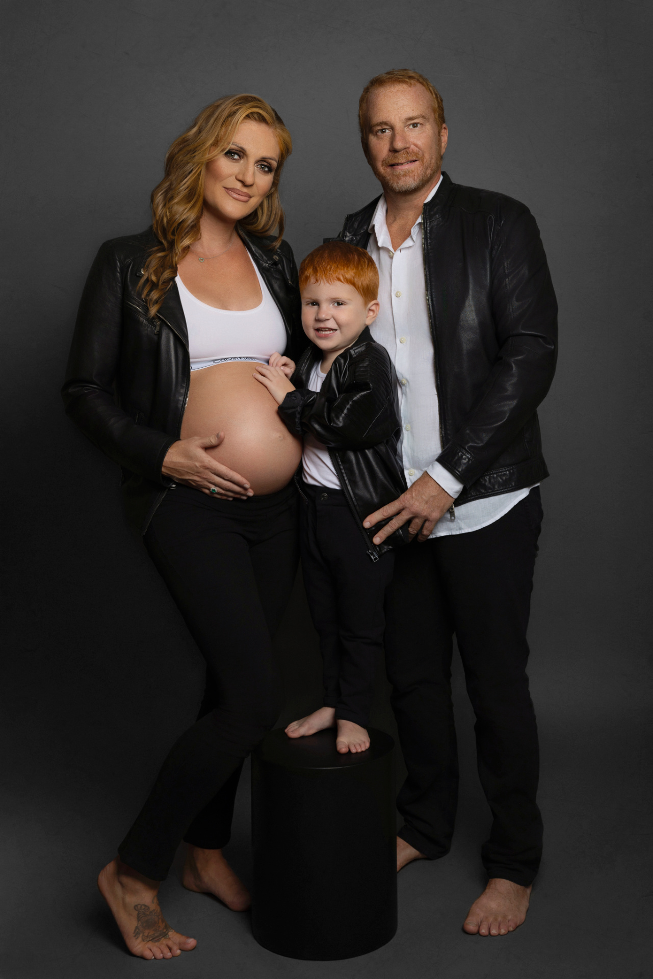 Servizio fotografico di famiglia a Bologna con Claudia Spaziani: coppia con bambino e donna incinta in giacca di pelle nera, look coordinato e atmosfera affettuosa.