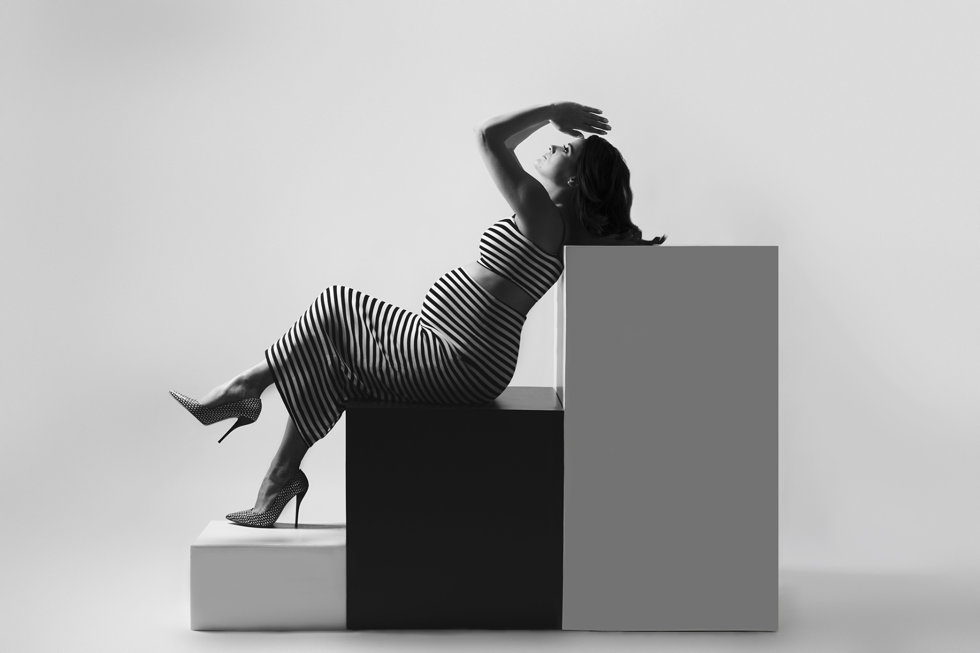 Ritratto artistico di maternità a Bologna realizzato da Claudia Spaziani: donna incinta in abito a righe bianche e nere, posa geometrica su blocchi scenografici, stile minimalista e fashion.