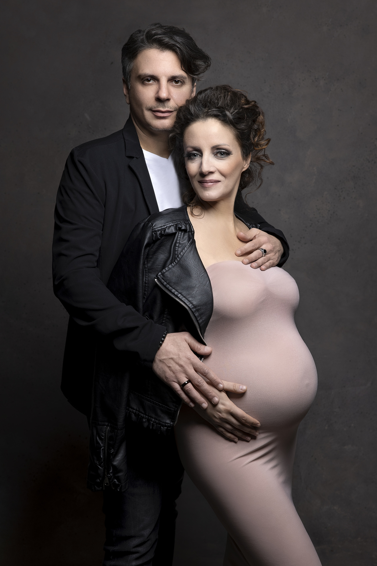 Ritratto di coppia maternità a Bologna realizzato da Claudia Spaziani: donna incinta in abito rosa e partner in giacca nera, posa affettuosa e raffinata.