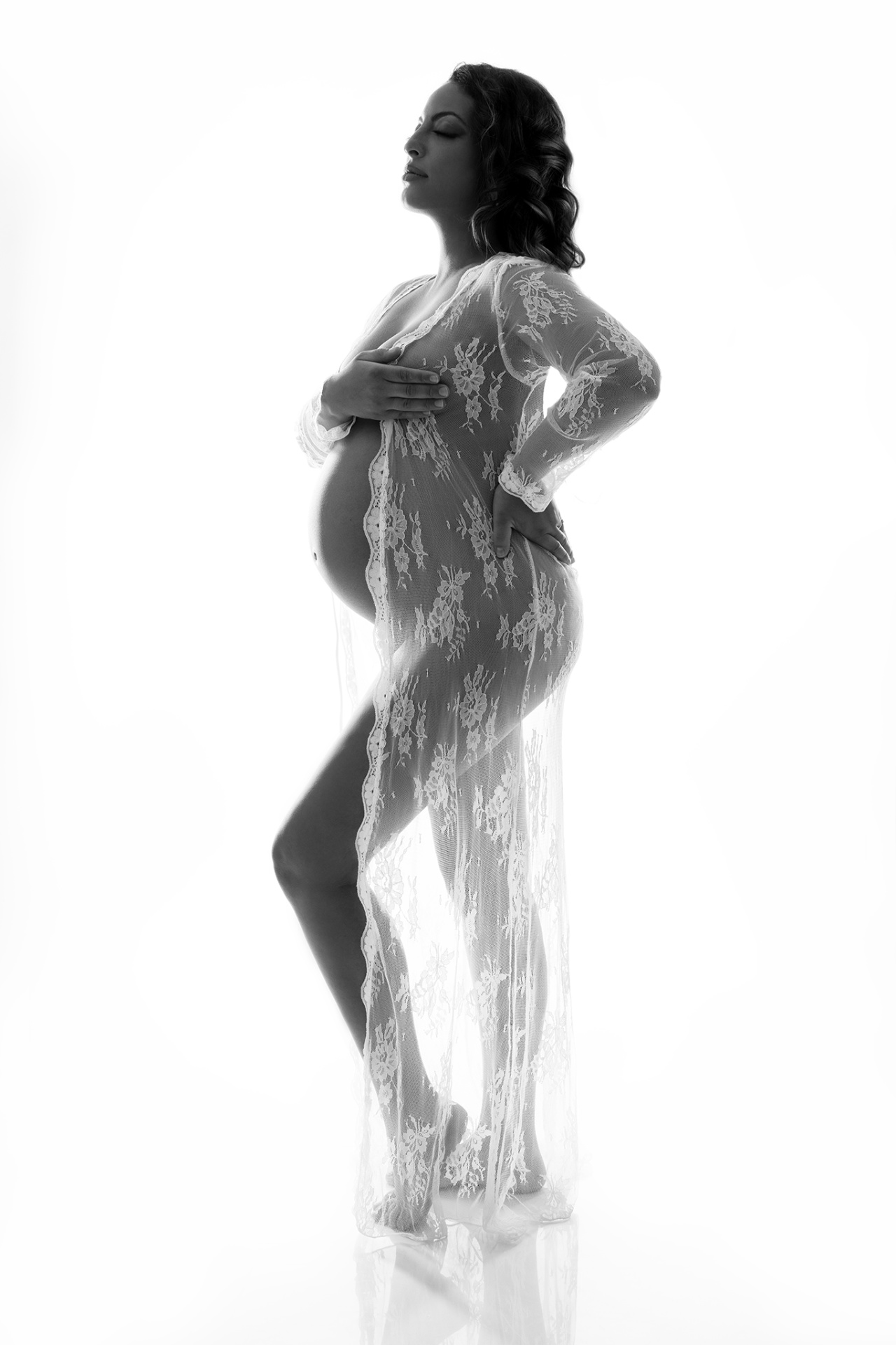 Ritratto di maternità in bianco e nero a Bologna realizzato da Claudia Spaziani: donna incinta in robe di pizzo trasparente, posa elegante e luce retroilluminata.