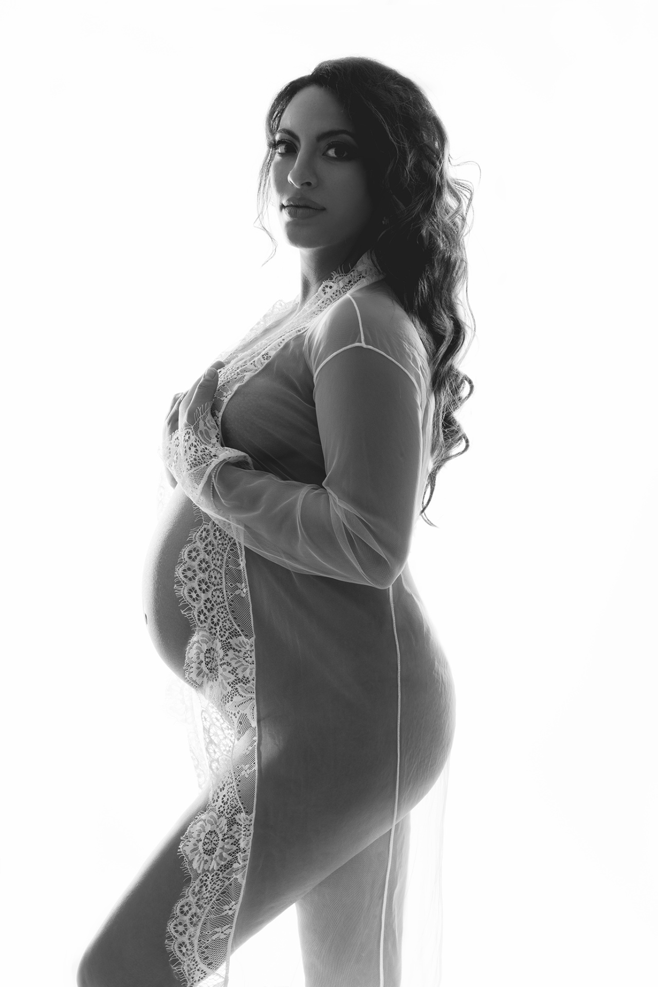 Foto maternità a Bologna con Claudia Spaziani: donna incinta in robe trasparente, posa di profilo e luce intensa, atmosfera eterea.