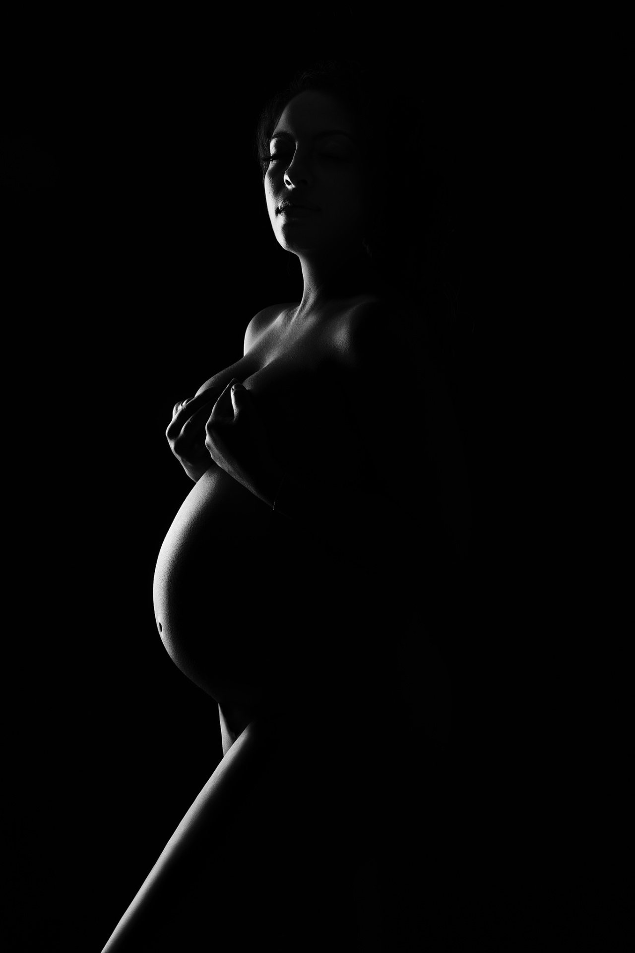 Ritratto artistico di maternità a Bologna firmato Claudia Spaziani: donna incinta nuda in profilo con luce intensa, atmosfera intima e potente.