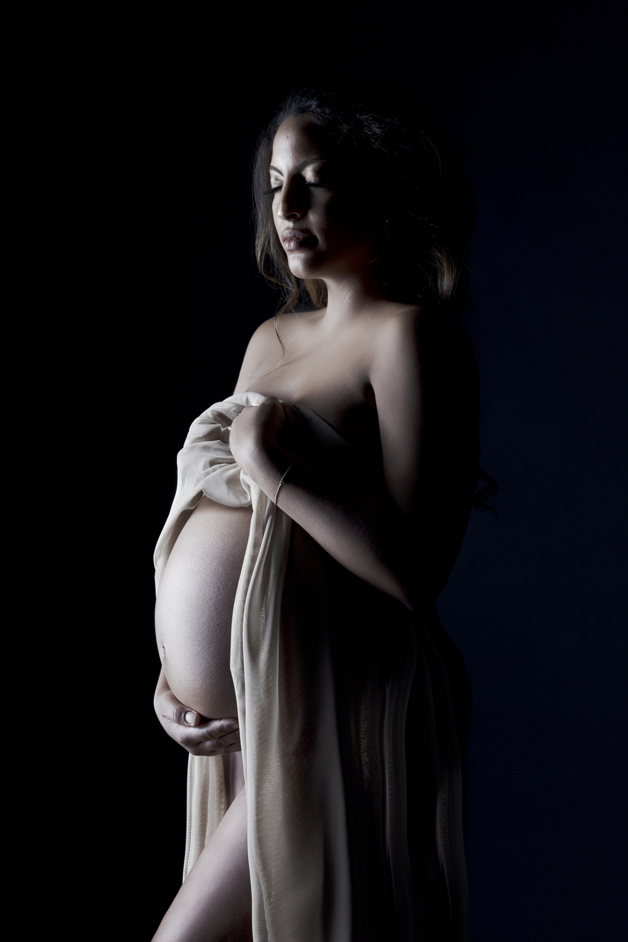 Foto maternità a Bologna con Claudia Spaziani: donna incinta avvolta in tessuto trasparente, posa intima e luce soffusa.