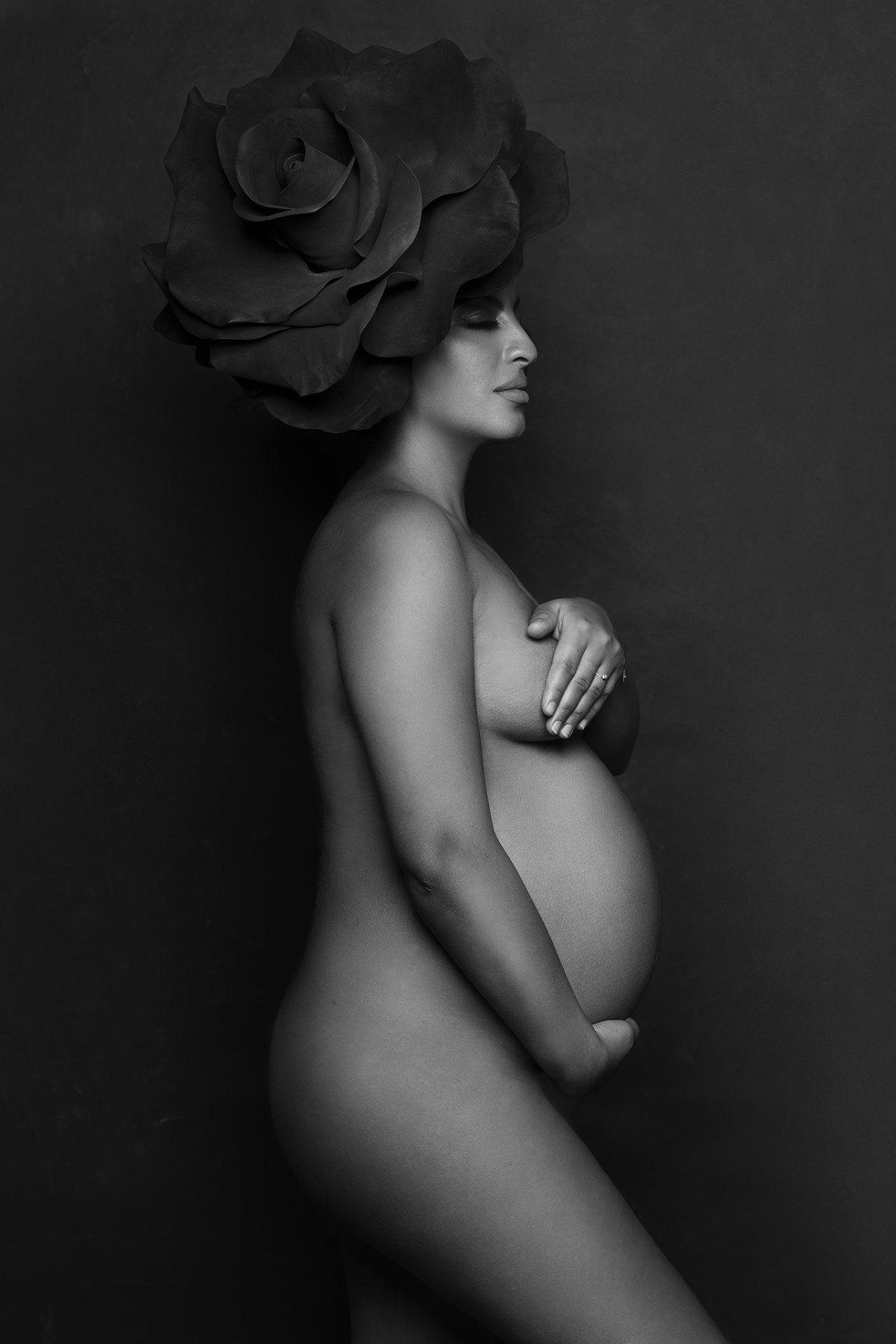 Foto artistica di maternità in bianco e nero a Bologna firmata Claudia Spaziani: donna incinta con copricapo floreale scenografico, posa simbolica e raffinata.