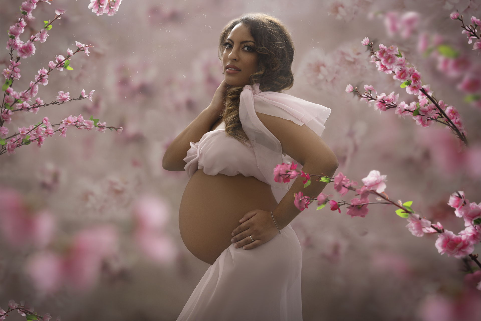 Ritratto di maternità a Bologna realizzato da Claudia Spaziani: donna incinta in abito rosa tra fiori di ciliegio, atmosfera naturale e poetica.