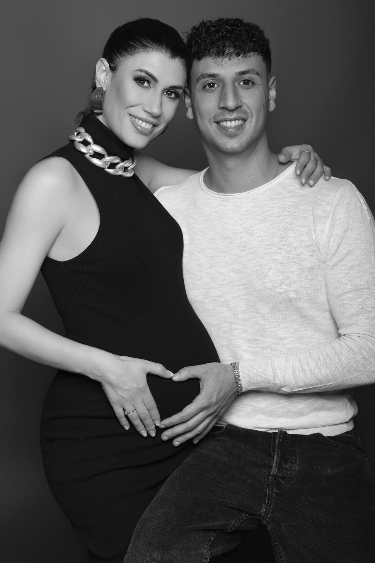Foto di coppia maternità in bianco e nero a Bologna con Claudia Spaziani: mani a cuore sul ventre, posa affettuosa e sorridente.