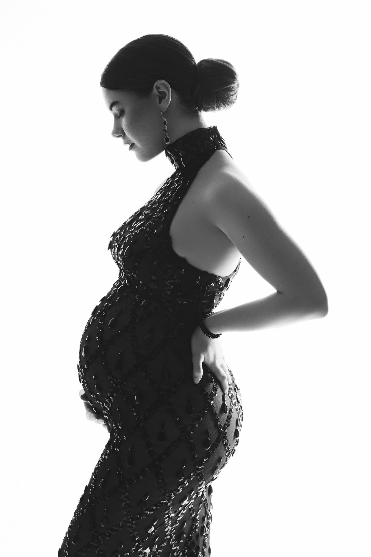 Foto maternità in bianco e nero a Bologna con Claudia Spaziani: donna incinta in abito aderente con motivo, posa di profilo elegante e luce drammatica.