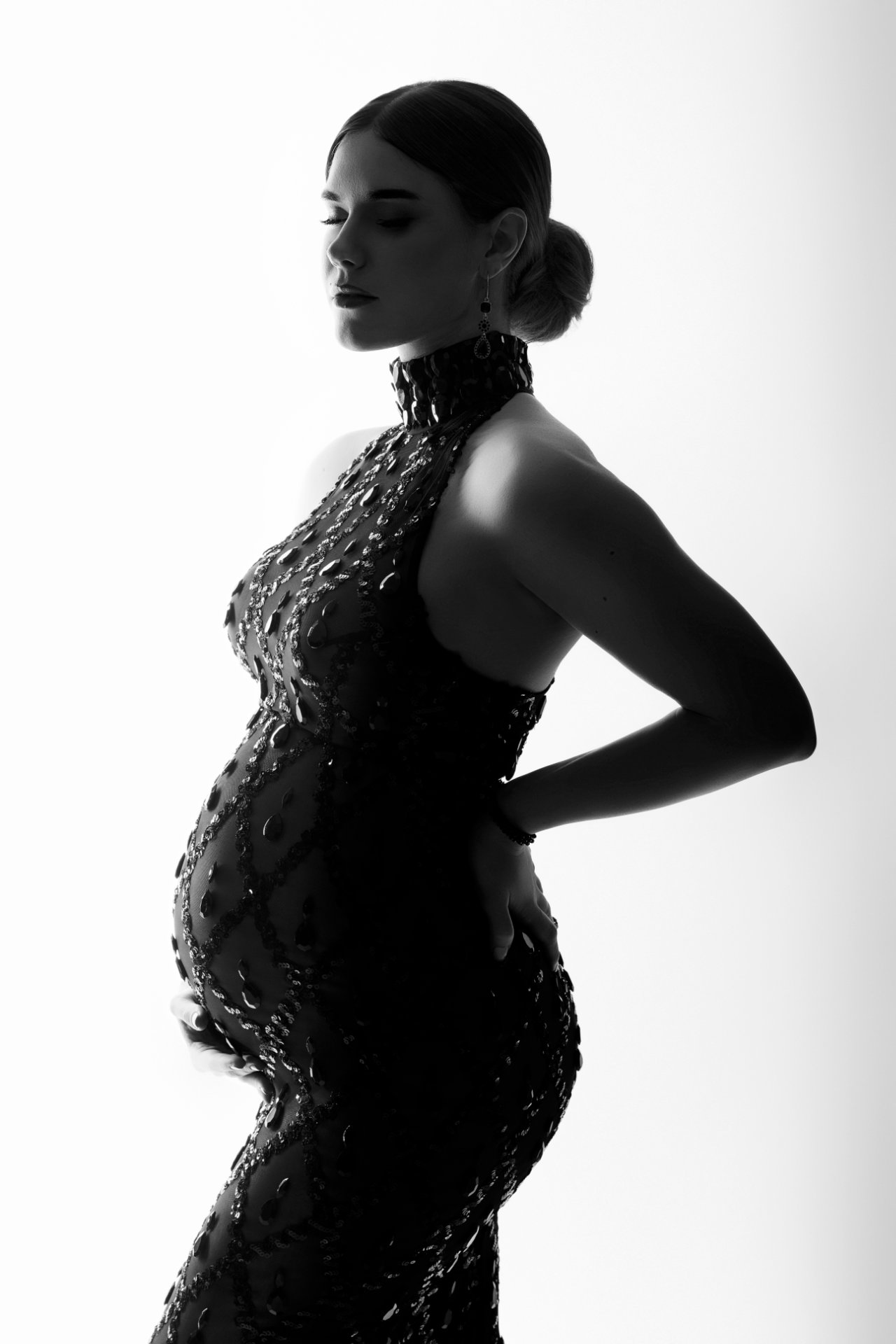 Ritratto artistico di maternità in bianco e nero a Bologna firmato Claudia Spaziani: donna incinta in abito scintillante, posa elegante e luce retroilluminata.