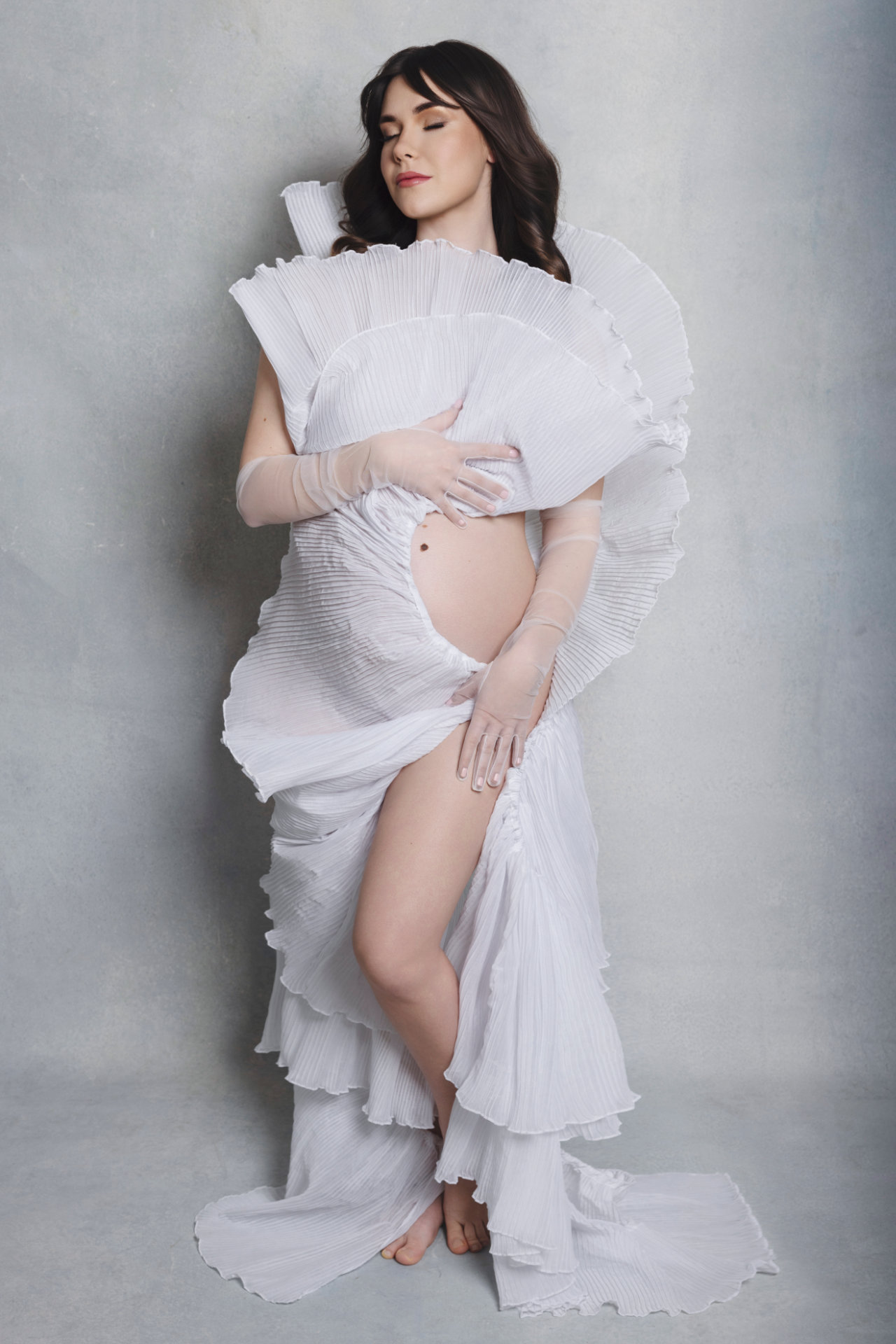 Ritratto di maternità a Bologna realizzato da Claudia Spaziani: donna incinta in abito bianco scultoreo con pieghe architettoniche, posa elegante e raffinata.