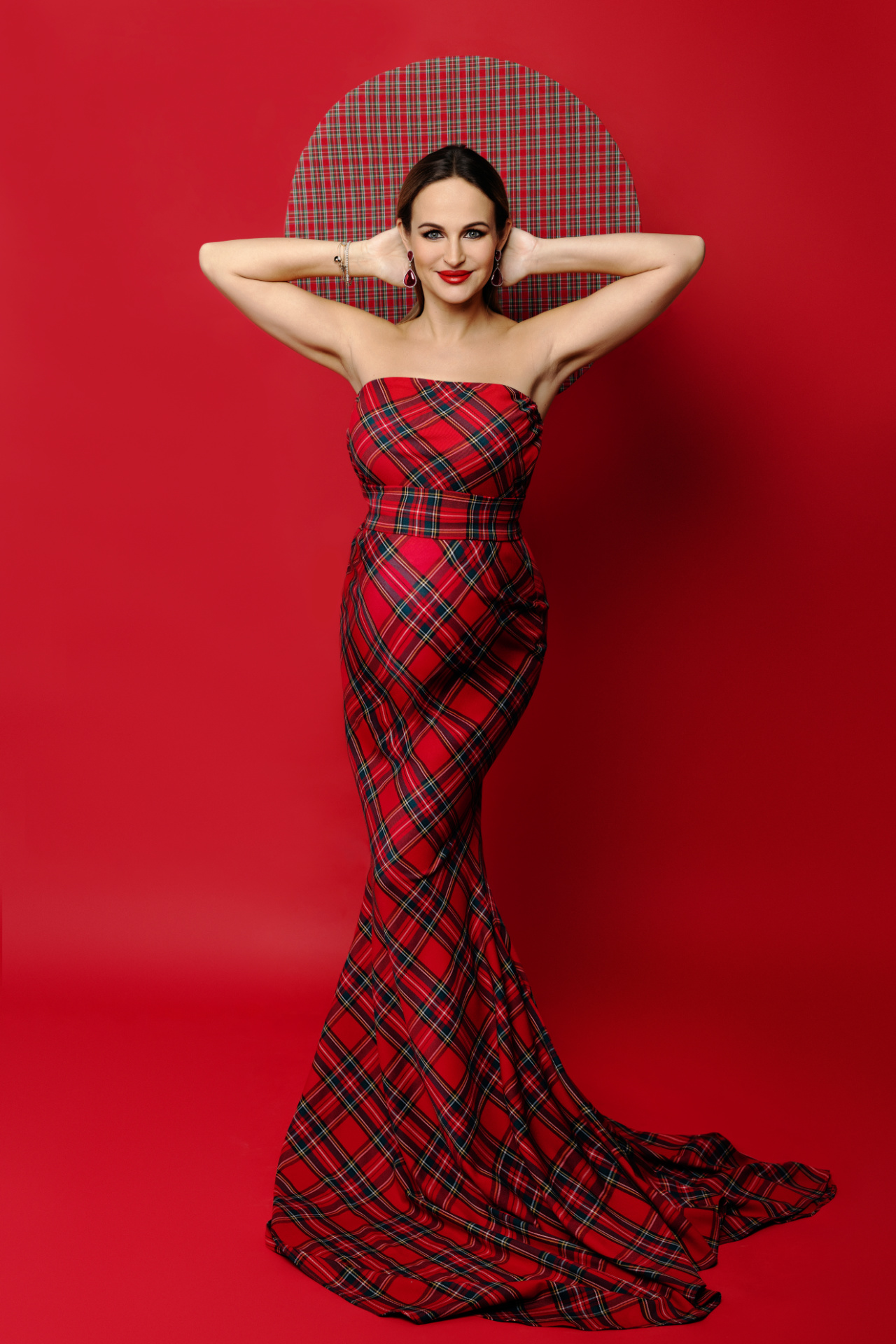 Ritratto di maternità a Bologna realizzato da Claudia Spaziani: donna incinta in abito tartan rosso con backdrop coordinato, posa sorridente e atmosfera scenografica.