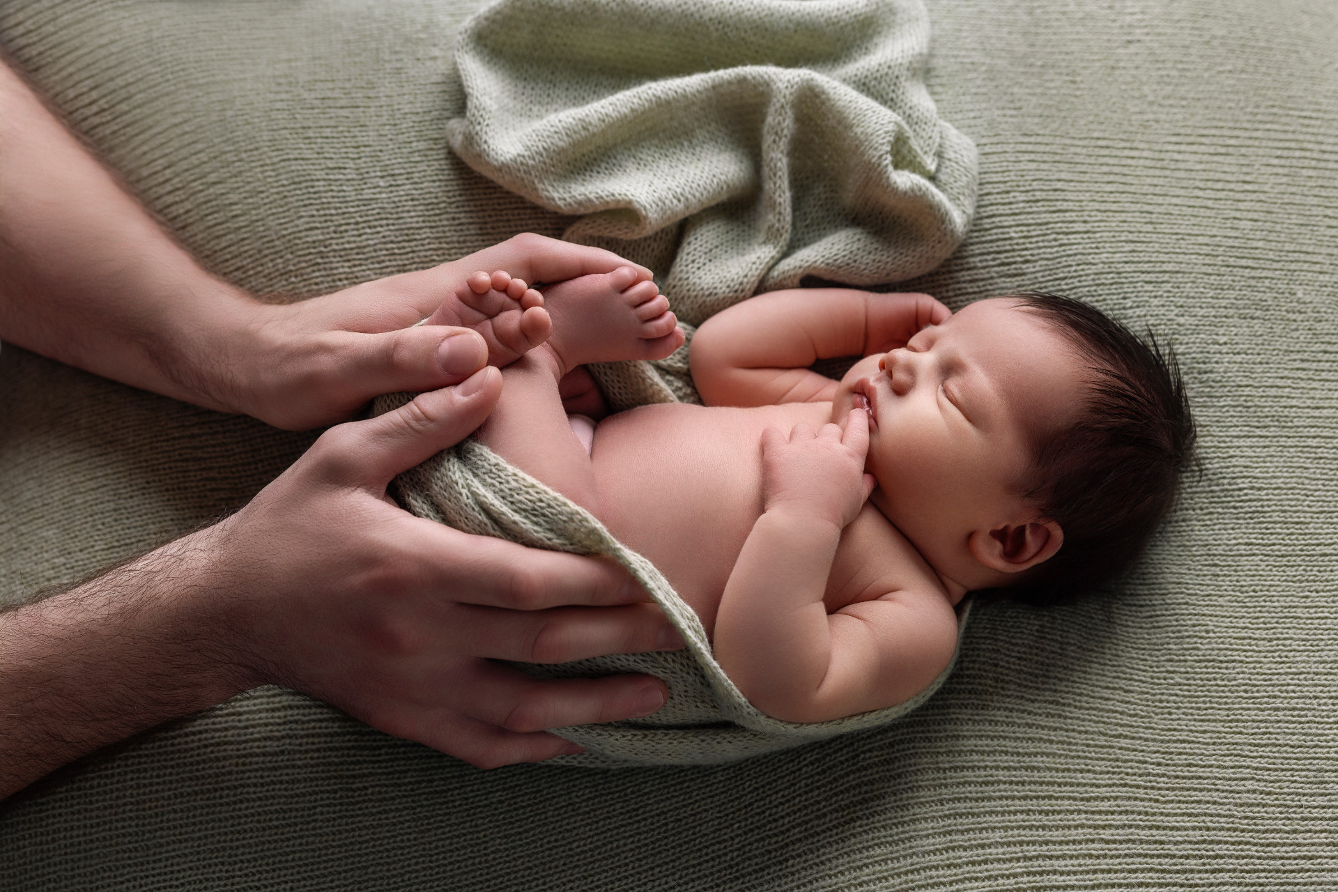 Fotografia newborn a Bologna realizzata da Claudia Spaziani: neonato che riposa su coperta verde, con la testa sorretta da mani protettive.