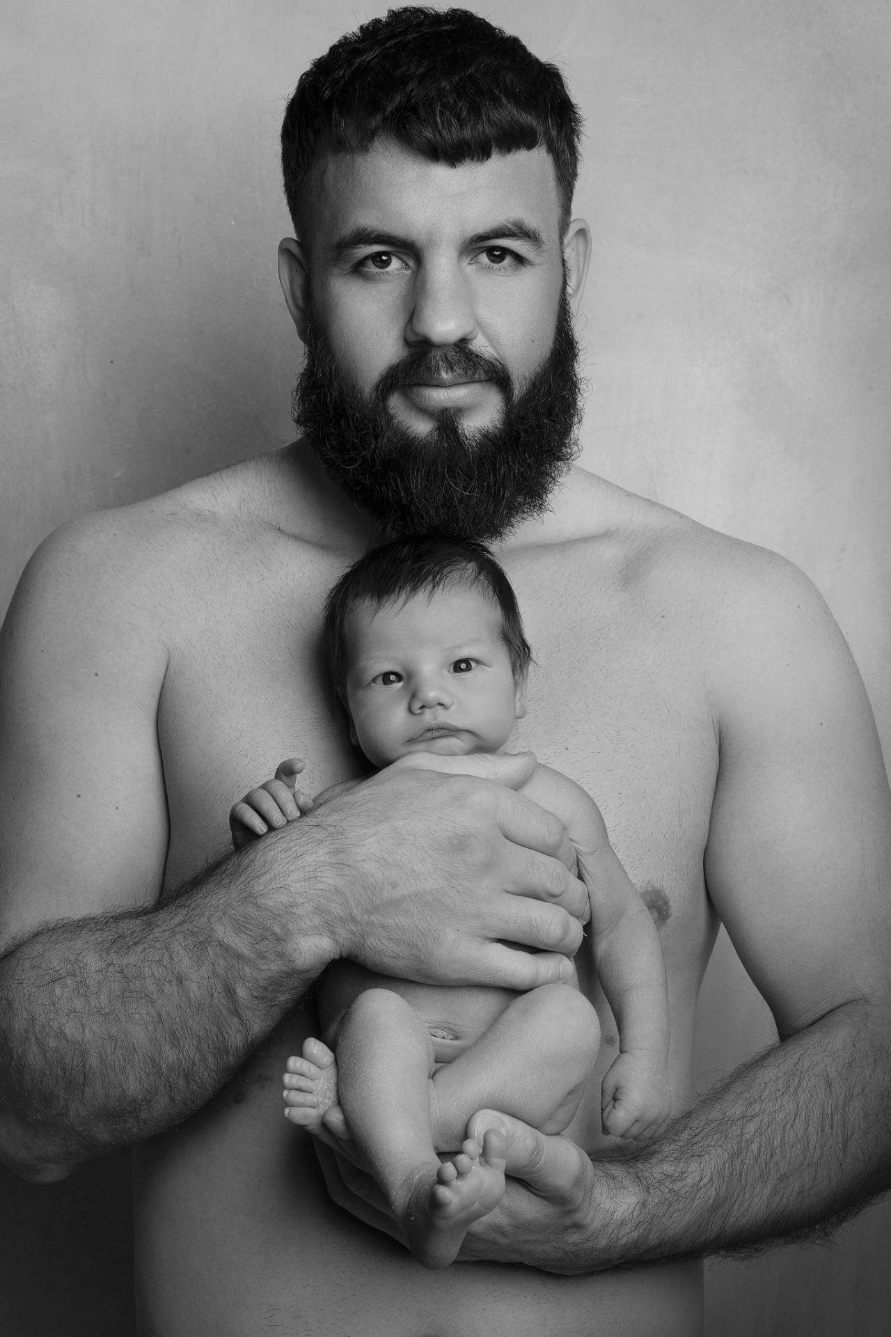 Claudia Spaziani fotografa newborn a Bologna: ritratto in bianco e nero di papà con barba che tiene in braccio il neonato.