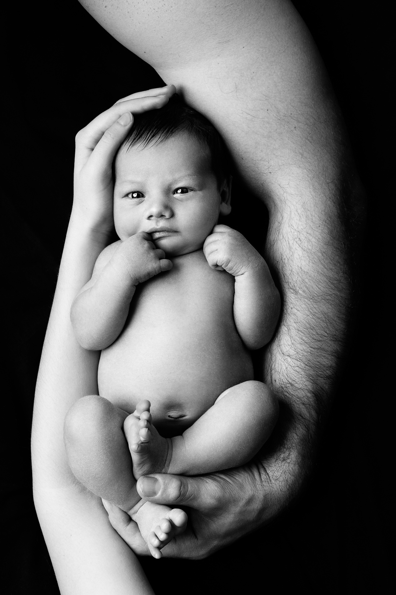 Claudia Spaziani fotografa newborn a Bologna: ritratto in bianco e nero di neonato cullato tra le braccia di due adulti.