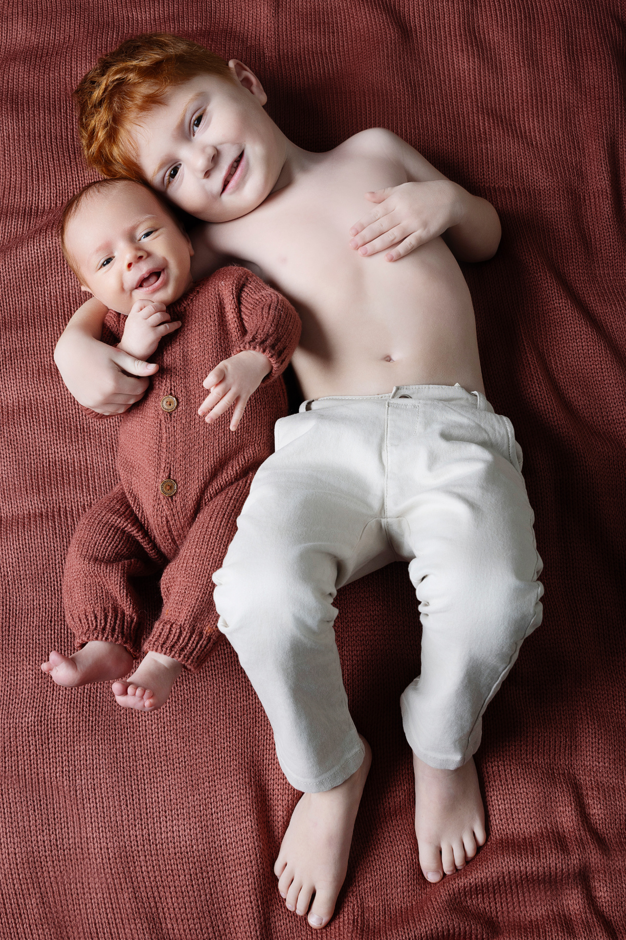 Foto di fratello maggiore con neonato maschio in abito marrone, scattata nello studio fotografico di Claudia Spaziani a Bologna. Immagine che esalta legame familiare e tenerezza.