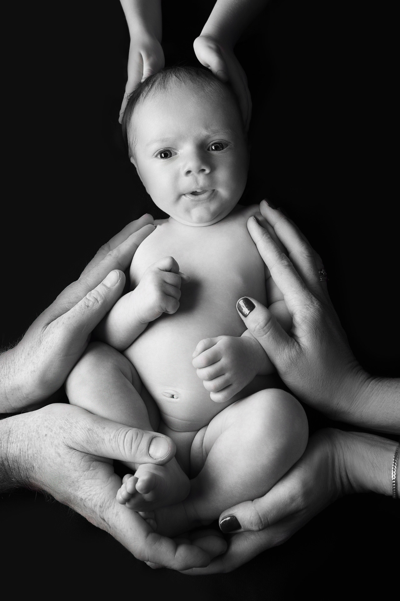 Fotografia artistica in bianco e nero di neonato maschio sorretto da mani adulte, scattata da Claudia Spaziani fotografa a Bologna. Immagine intensa che simboleggia protezione, amore e sostegno familiare.