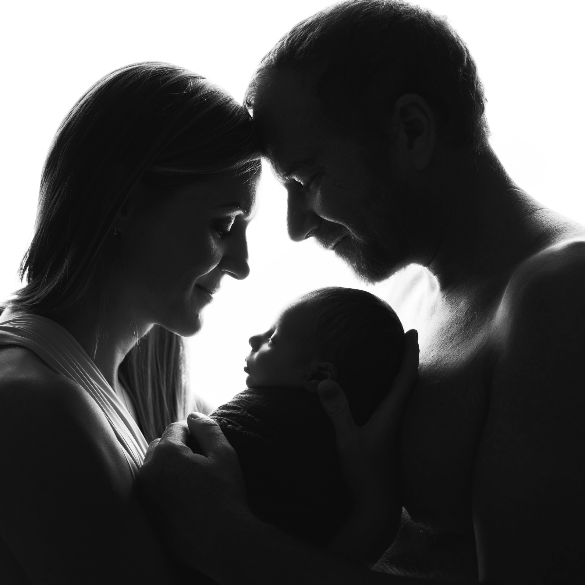 Fotografia in bianco e nero di genitori che cullano neonato maschio, scattata da Claudia Spaziani fotografa a Bologna. Immagine artistica e affettuosa.