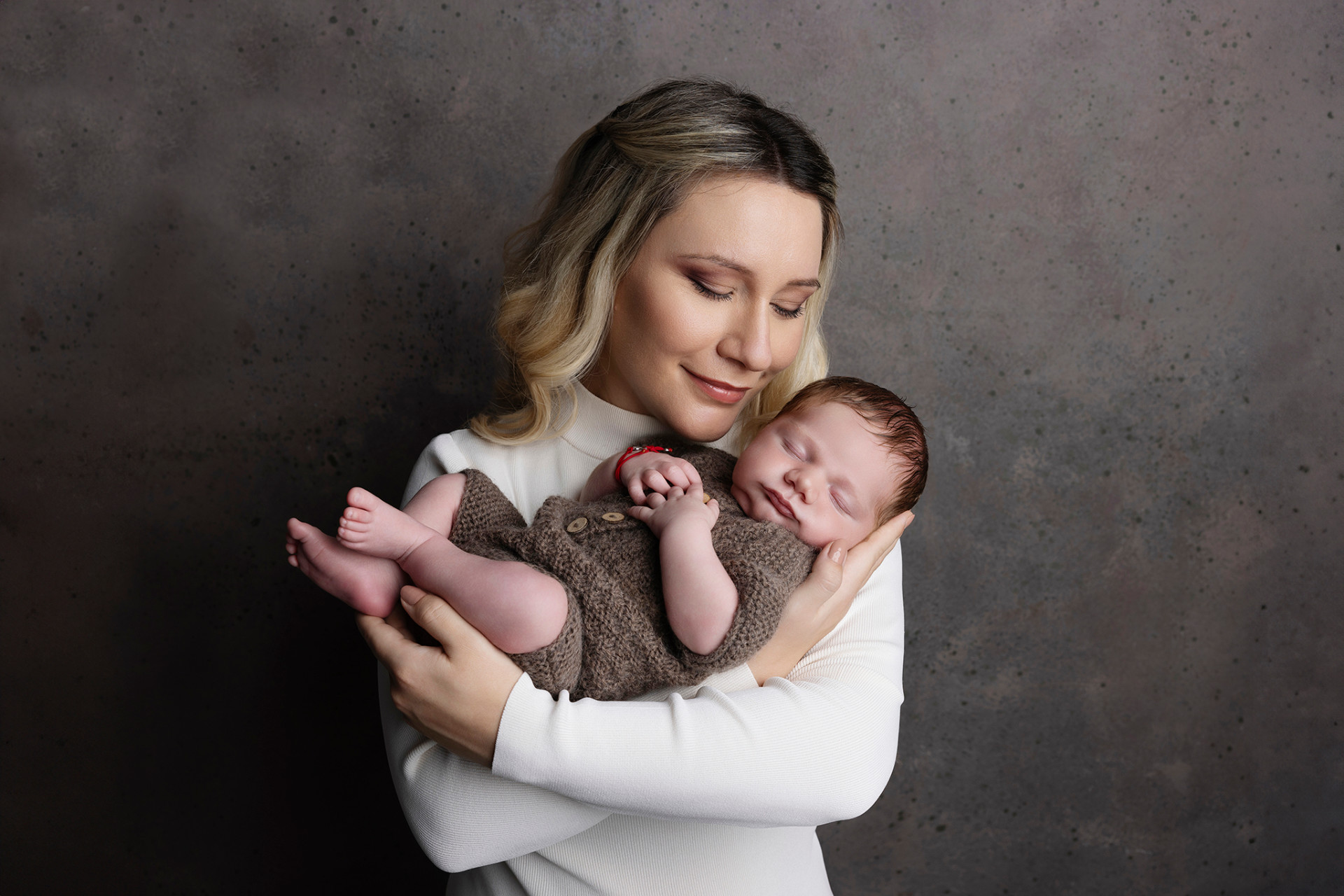 Foto intima di madre che culla neonato maschio in outfit marrone, scattata da Claudia Spaziani fotografa a Bologna. Immagine che trasmette dolcezza e protezione.