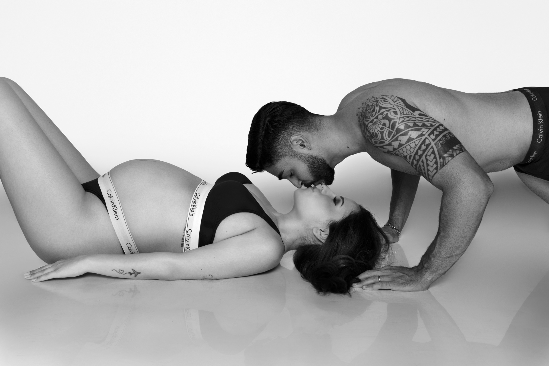 Donna incinta sdraiata in intimo Calvin Klein, baciata dal partner sopra di lei. Foto di maternità di Claudia Spaziani, Bologna.