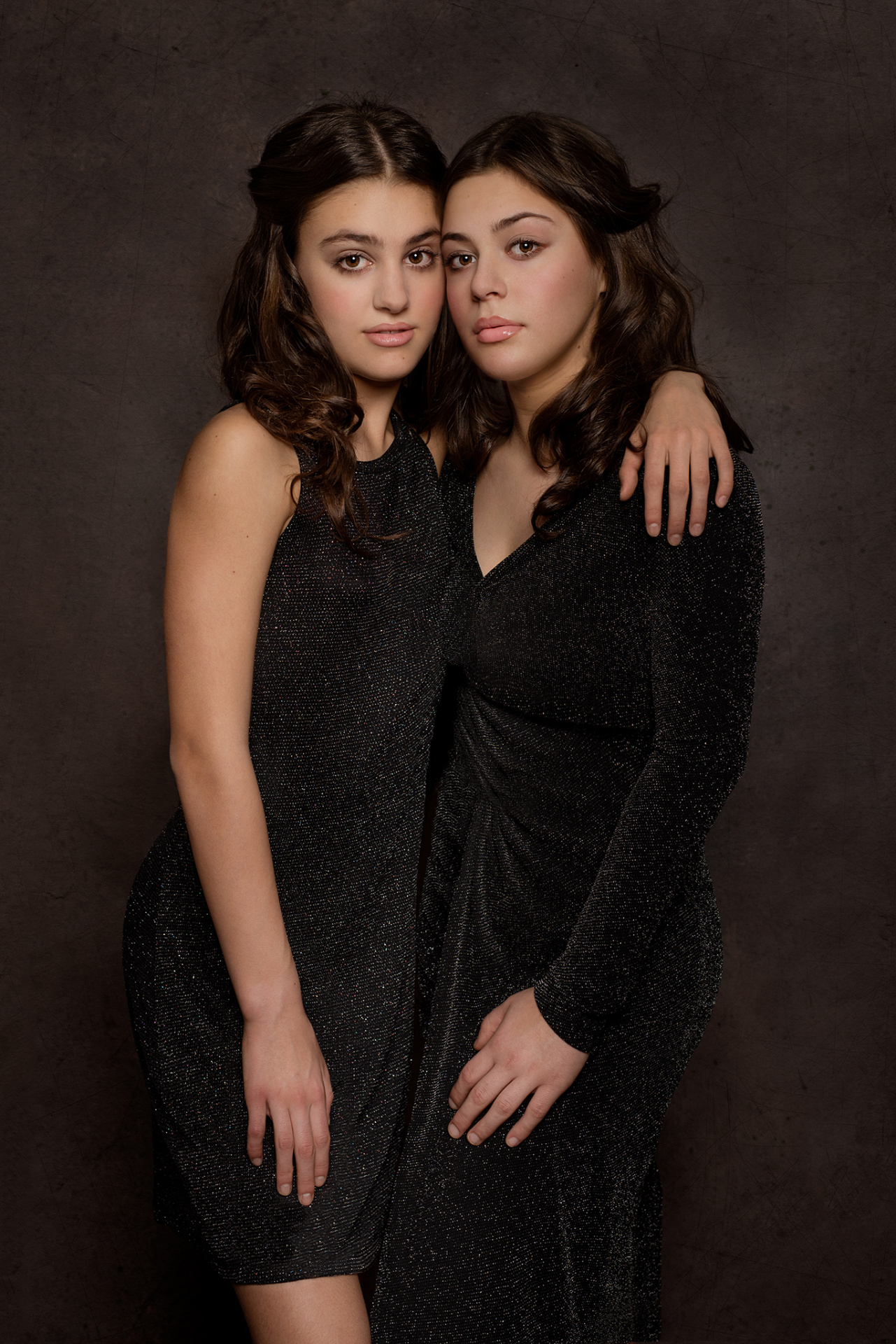 Due adolescenti in abiti neri brillanti, abbracciate in posa formale su sfondo scuro, ritratte da Claudia Spaziani a Bologna.