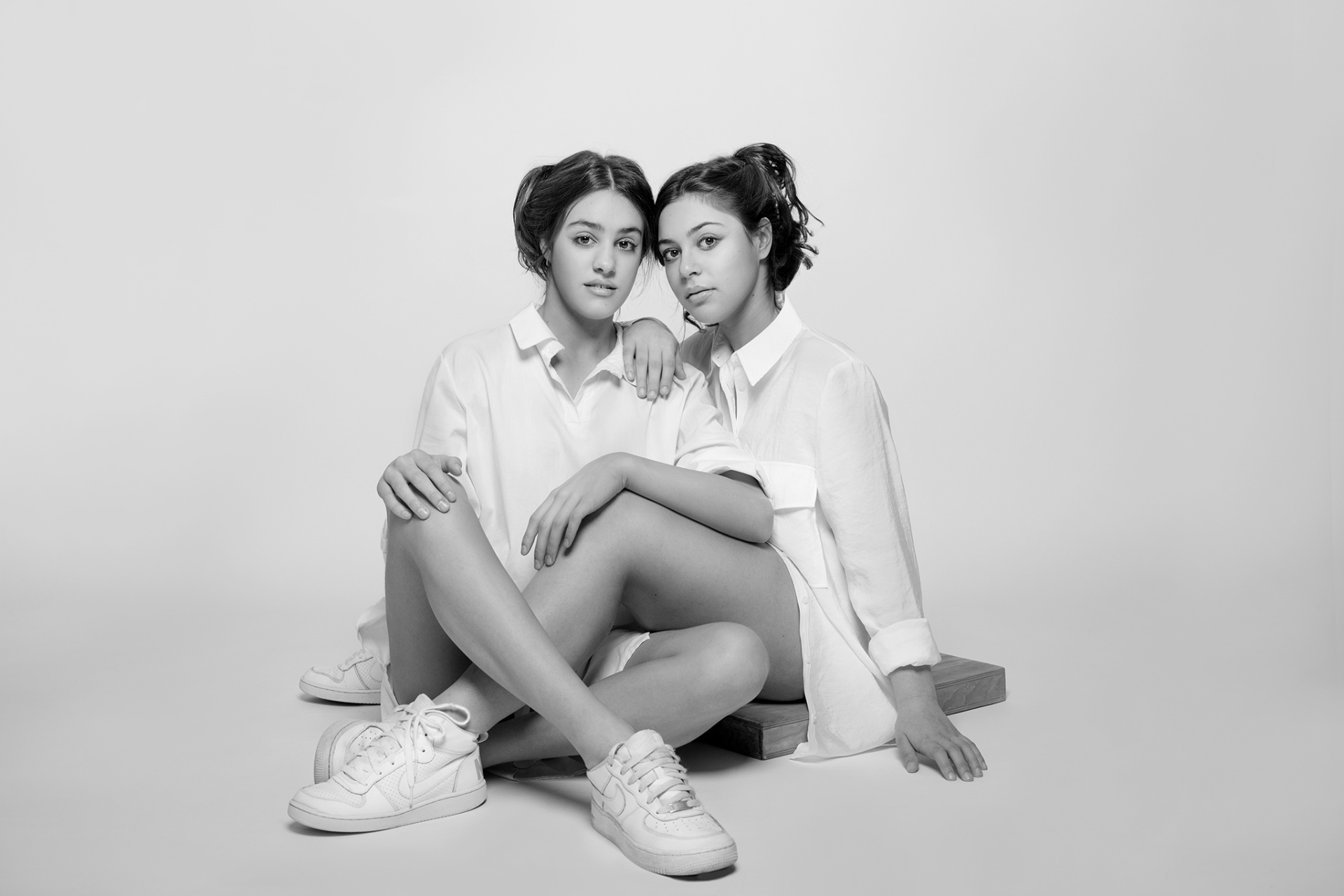 Due adolescenti sorridenti con fasce e maglie a maniche lunghe, abbracciate in posa simmetrica, ritratte in bianco e nero da Claudia Spaziani a Bologna.