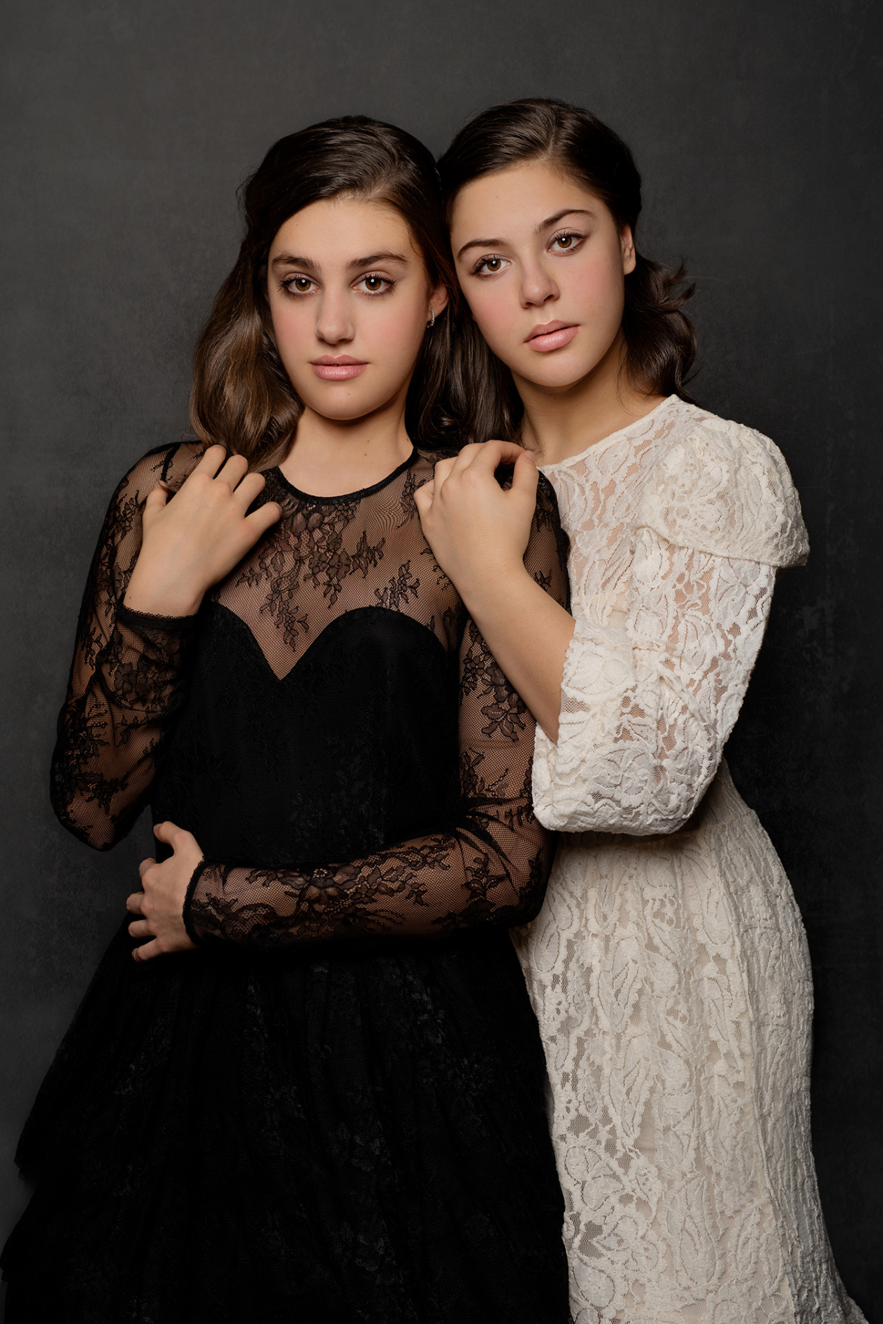 Ritratto elegante di due adolescenti in abiti in pizzo bianco e nero, in posa ravvicinata su sfondo neutro, realizzato da Claudia Spaziani nel suo studio fotografico a Bologna.