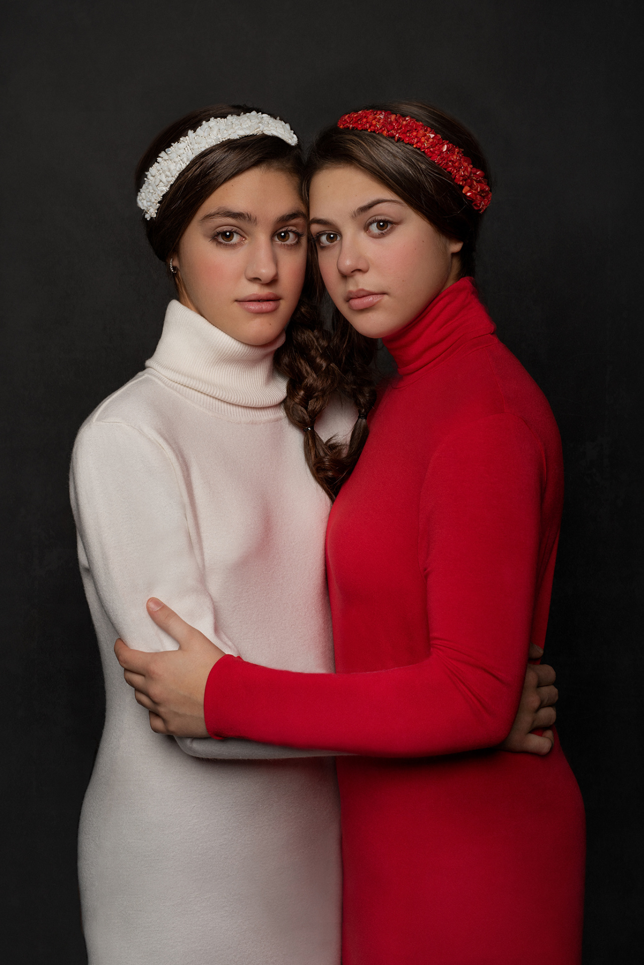 Due adolescenti in abiti coordinati rosso e bianco con trecce e fasce, abbracciate in posa simmetrica, fotografate da Claudia Spaziani nel suo studio a Bologna.