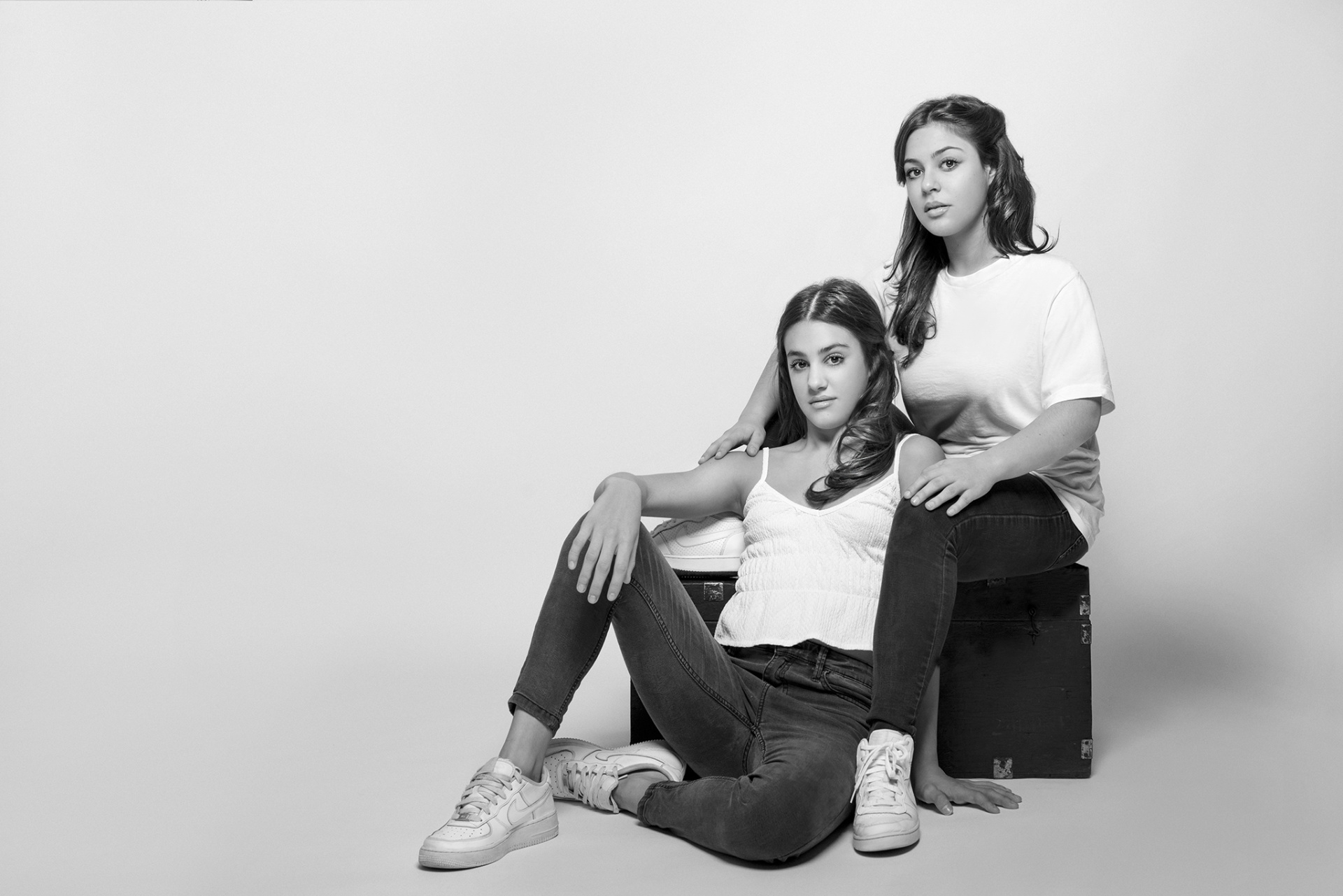 Ritratto monocromatico di due adolescenti in jeans e magliette bianche, seduti in posa affettuosa, fotografati da Claudia Spaziani nel suo studio a Bologna.