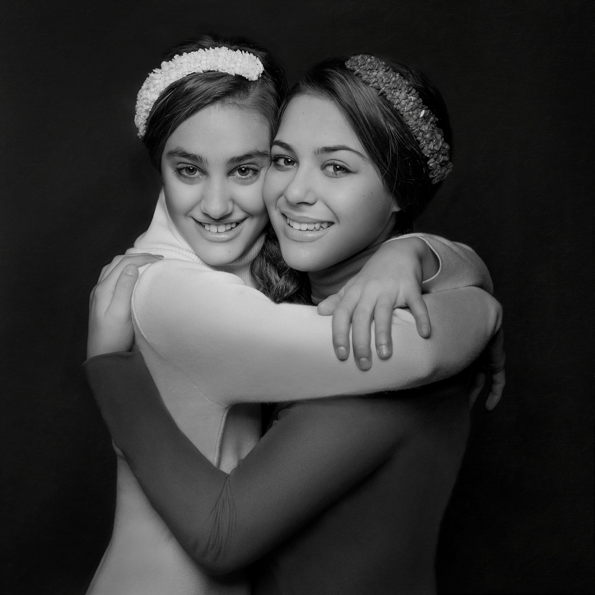 Due adolescenti sorridenti con fasce e maglie a maniche lunghe, abbracciate in posa simmetrica, ritratte in bianco e nero da Claudia Spaziani a Bologna.