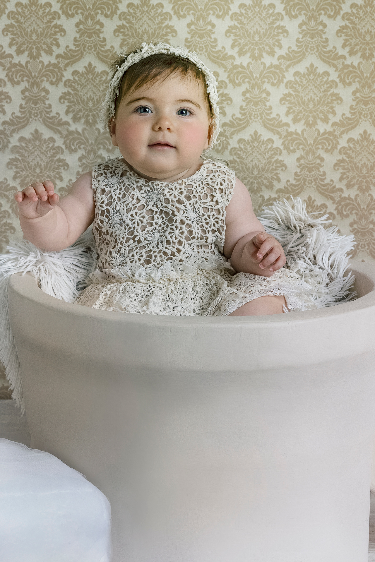 Ritratto elegante di bambina in abito crema con fascia in pizzo, seduta in contenitore cilindrico, scattato da Claudia Spaziani nel suo studio a Bologna.