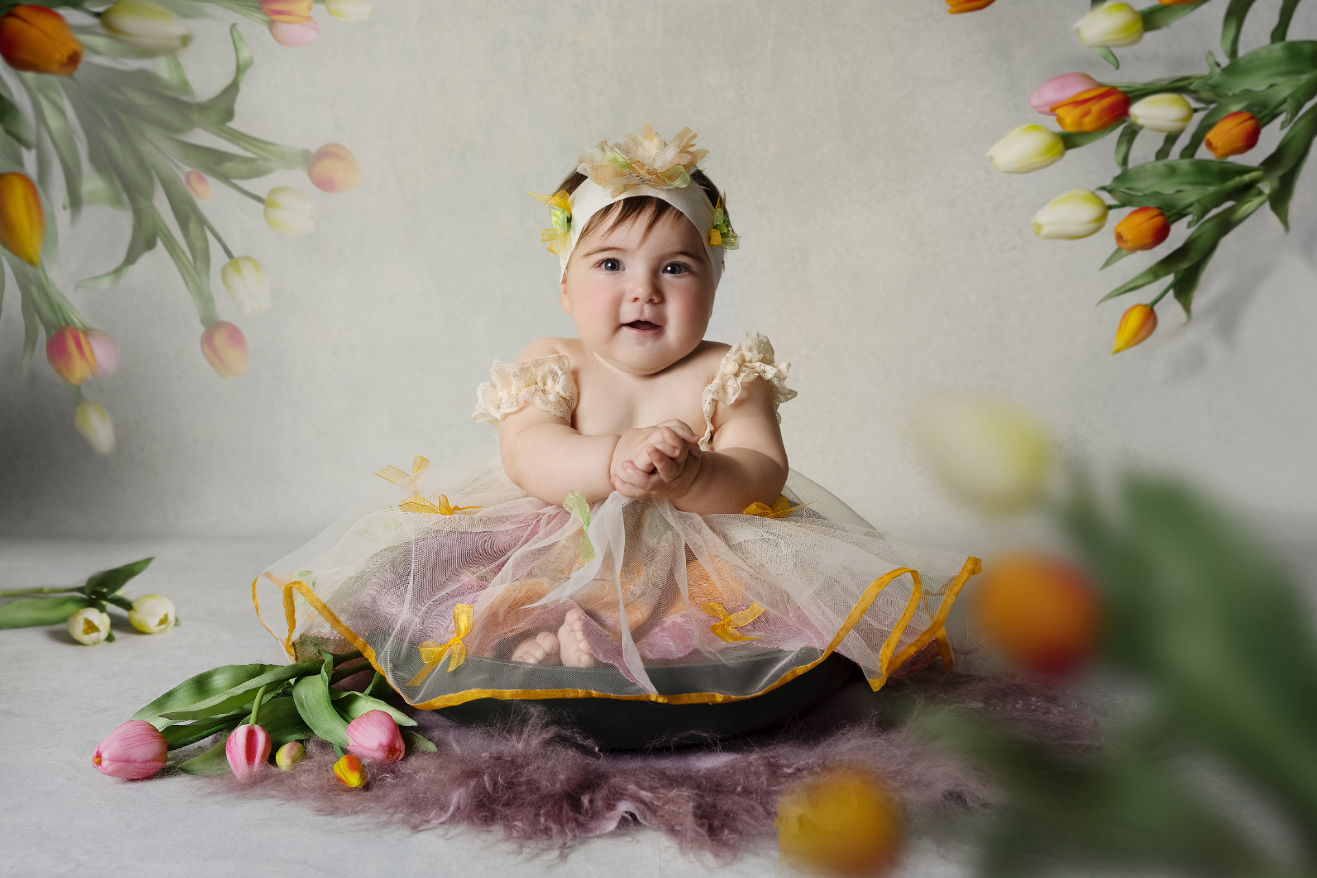 Foto creativa di bambina di 6 mesi in ciotola nera con abito frangiato e tulipani multicolore, scattata da Claudia Spaziani nel suo studio fotografico a Bologna.