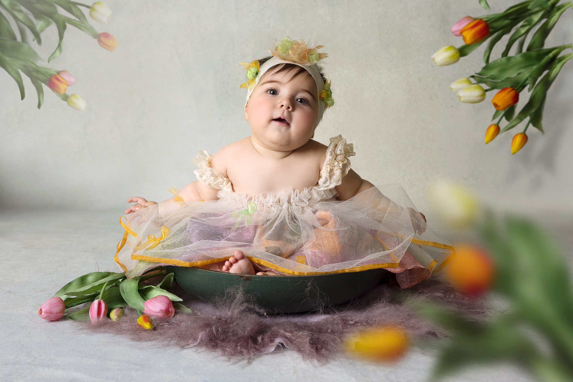 Foto artistica di bambina di 6 mesi in ciotola verde con tulipani colorati, ambientazione primaverile realizzata da Claudia Spaziani a Bologna.