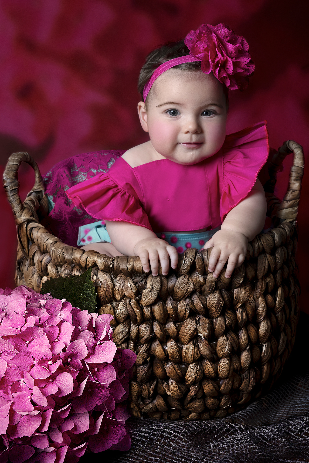 Ritratto in studio di bambina di 6 mesi in abito rosa con fascia floreale, accanto a ortensie rosa, realizzato da Claudia Spaziani a Bologna.