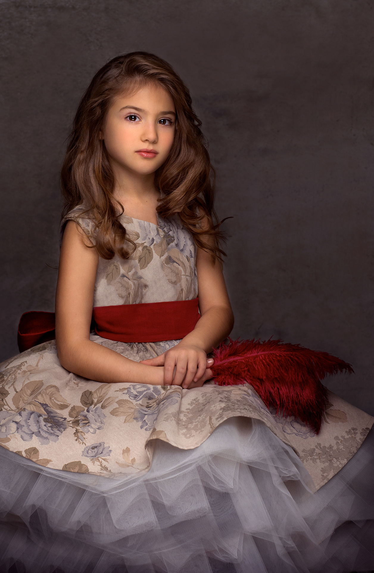 Ritratto classico di bambina in abito floreale con gonna in tulle e piume rosse, realizzato da Claudia Spaziani nel suo studio fotografico a Bologna.