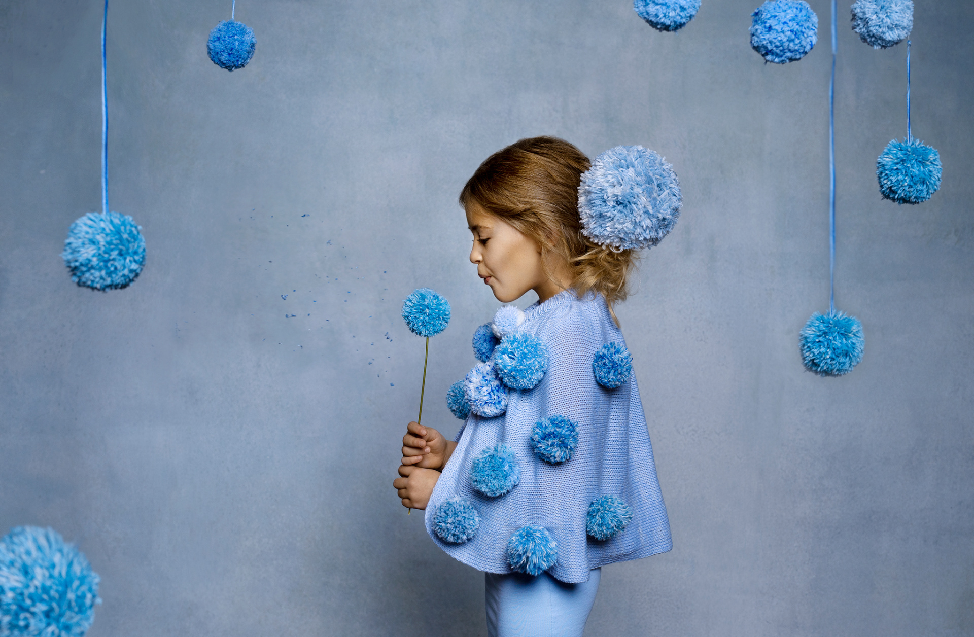 Ritratto artistico di bambina in outfit azzurro con pompon sospesi e bastoncino decorativo, scattato da Claudia Spaziani nel suo studio fotografico a Bologna.