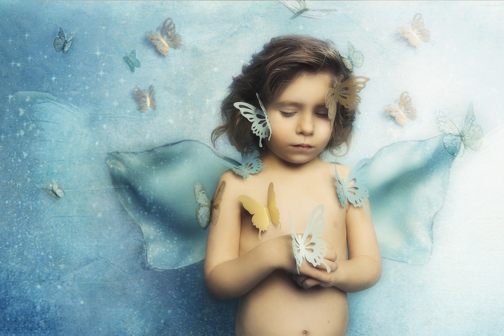 Ritratto fiabesco di bambino con ali traslucide e farfalle su sfondo azzurro, realizzato da Claudia Spaziani nel suo studio fotografico a Bologna.