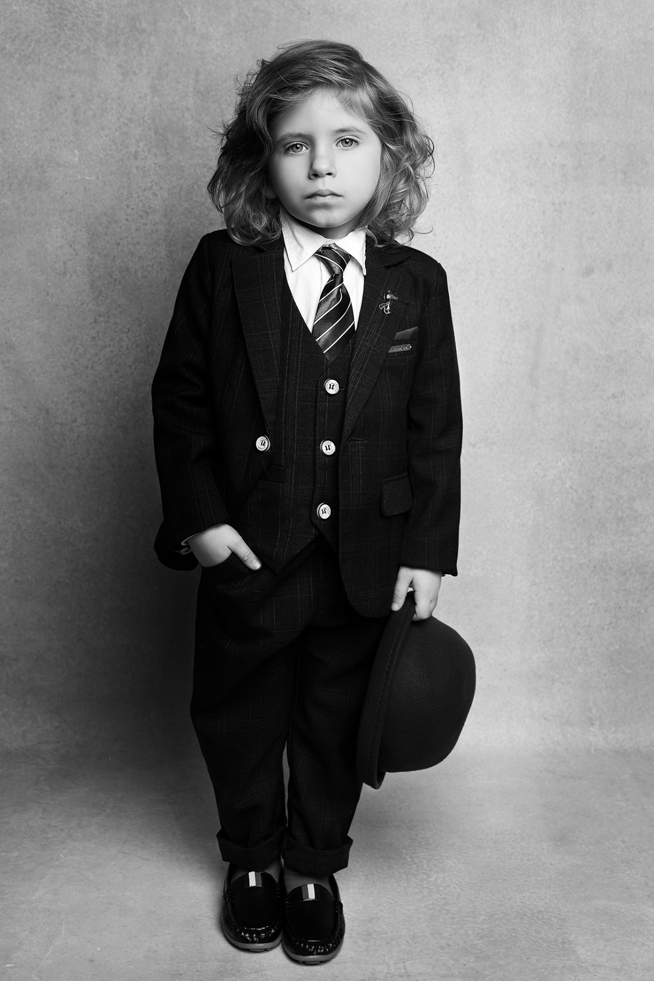 Ritratto in bianco e nero di bambino in completo elegante con bombetta, su sfondo neutro, scattato da Claudia Spaziani nel suo studio fotografico a Bologna.