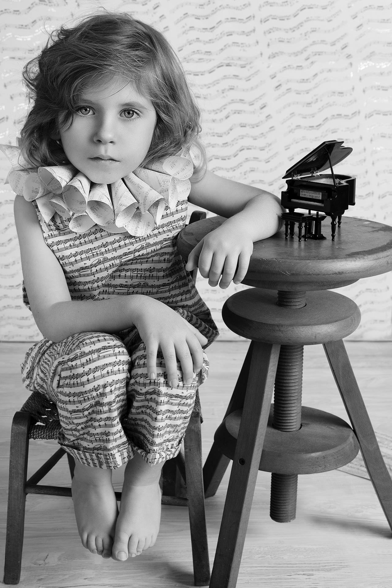 Ritratto in bianco e nero di bambino in abito decorato con note musicali e pianoforte in miniatura, scattato da Claudia Spaziani nel suo studio fotografico a Bologna.